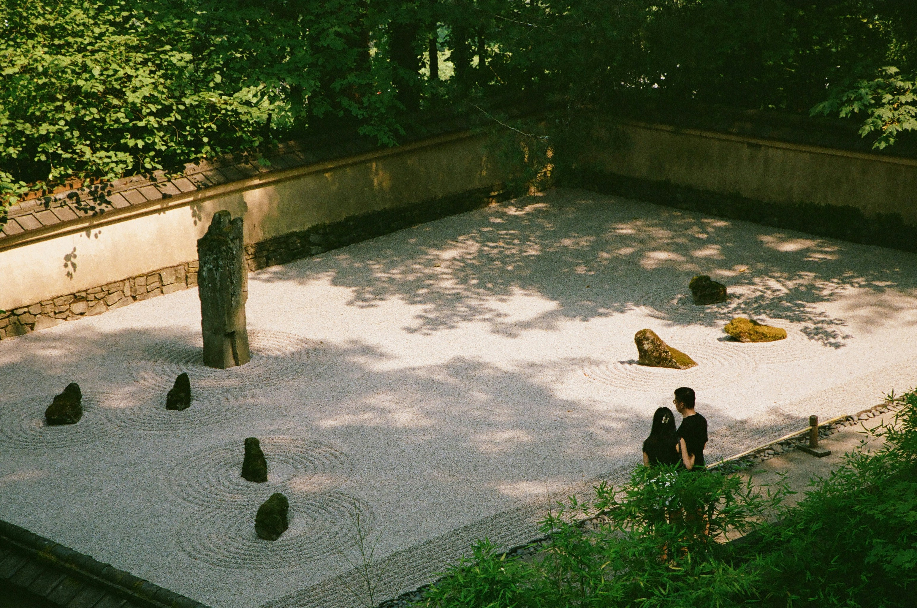 Two people standing by a raked gravel zen garden with mossy stones