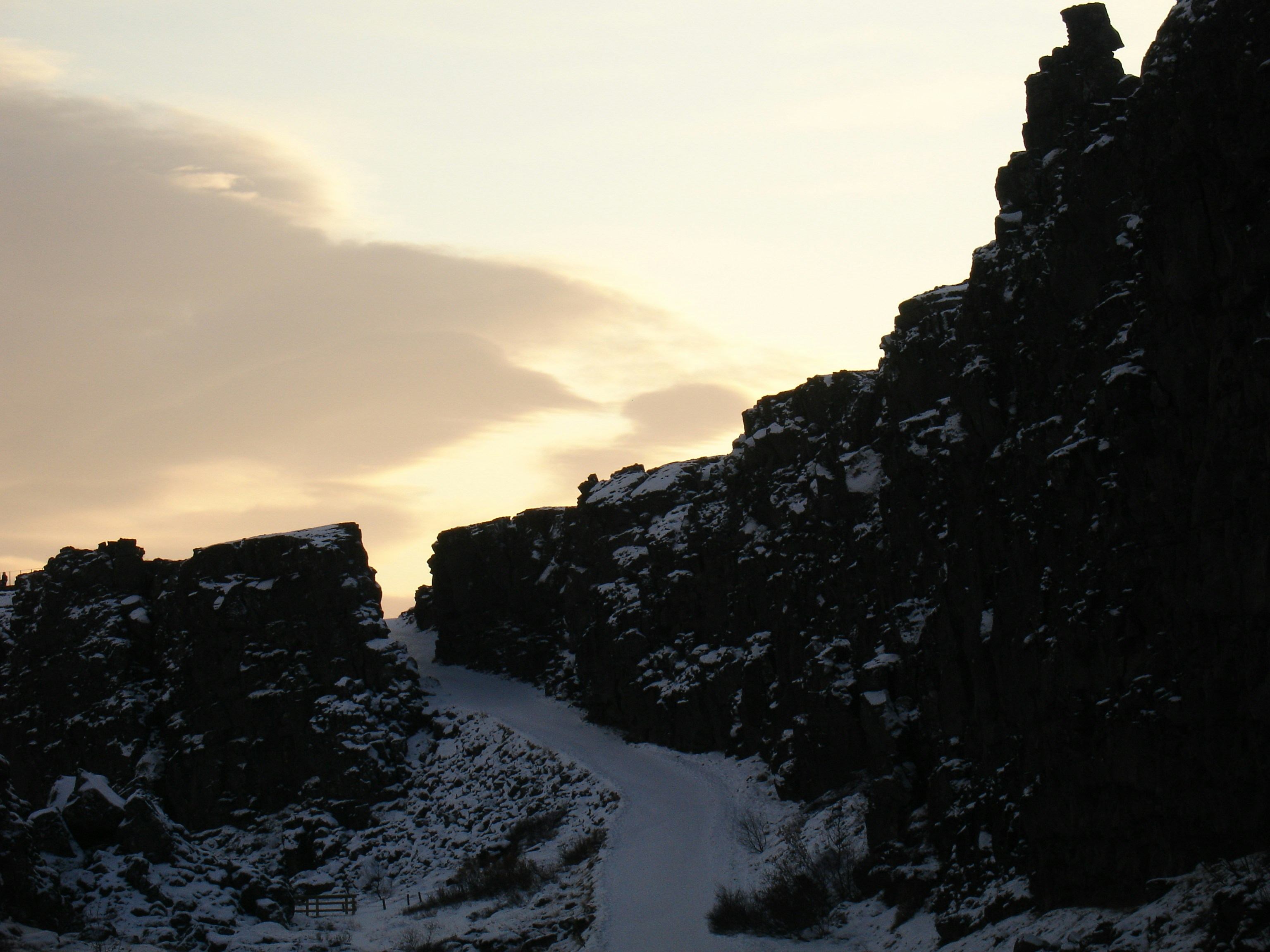 A snow-covered path between dark rocky cliffs under a pale sky