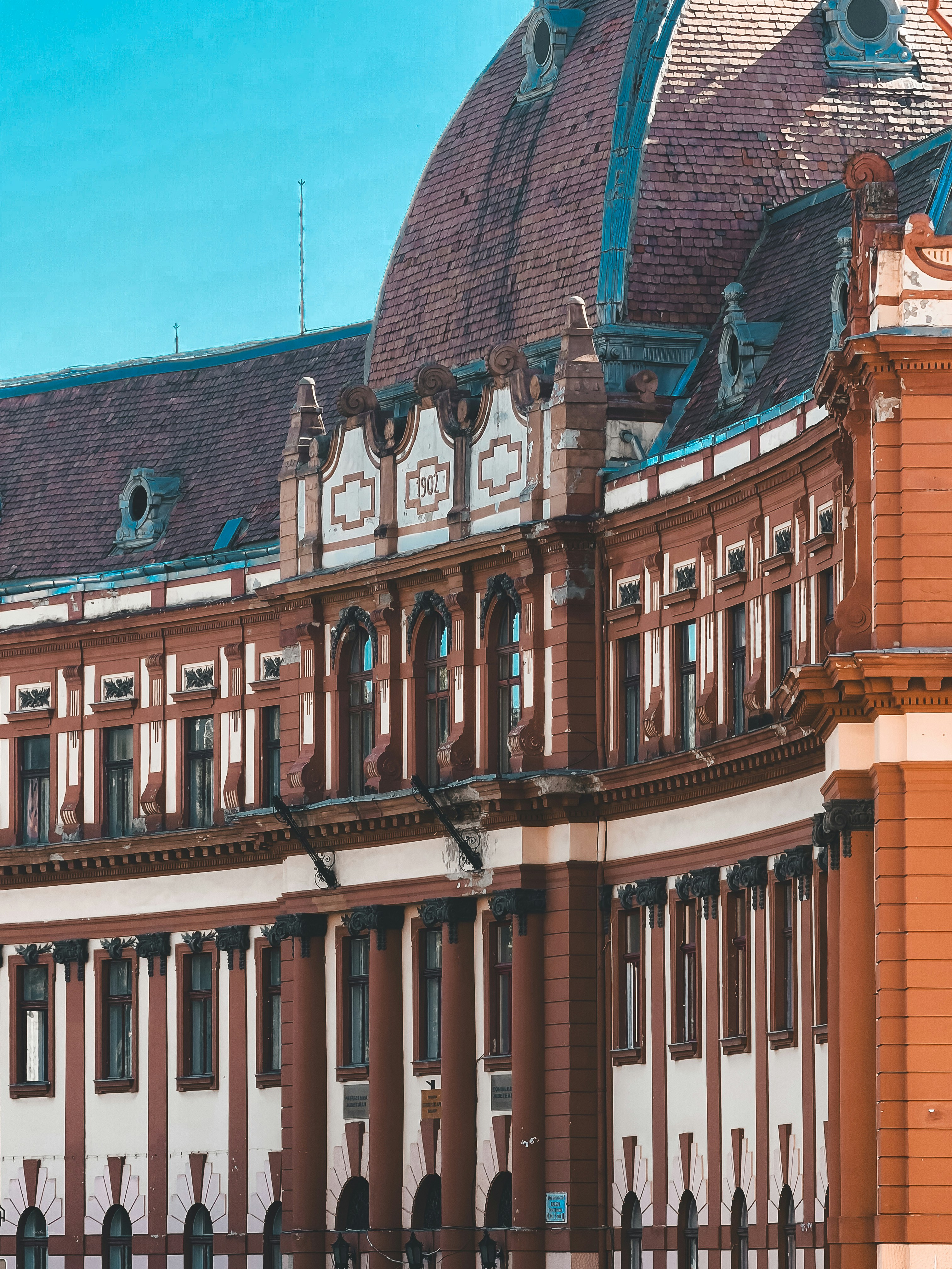 The ornate facade of a historic building with a curved roof and 1902 inscription