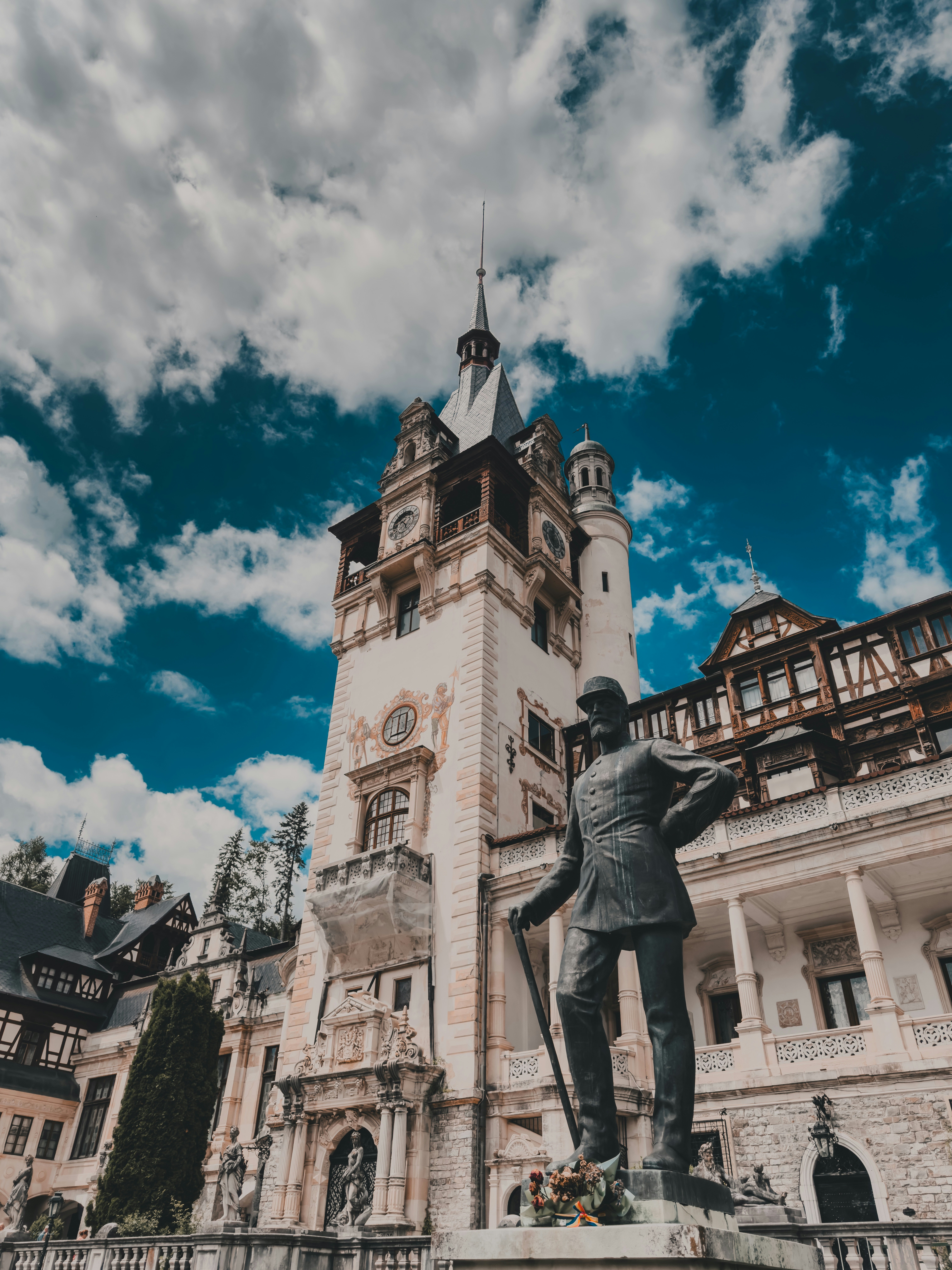 A bronze statue of a man in uniform before the ornate Peles Castle in Romania