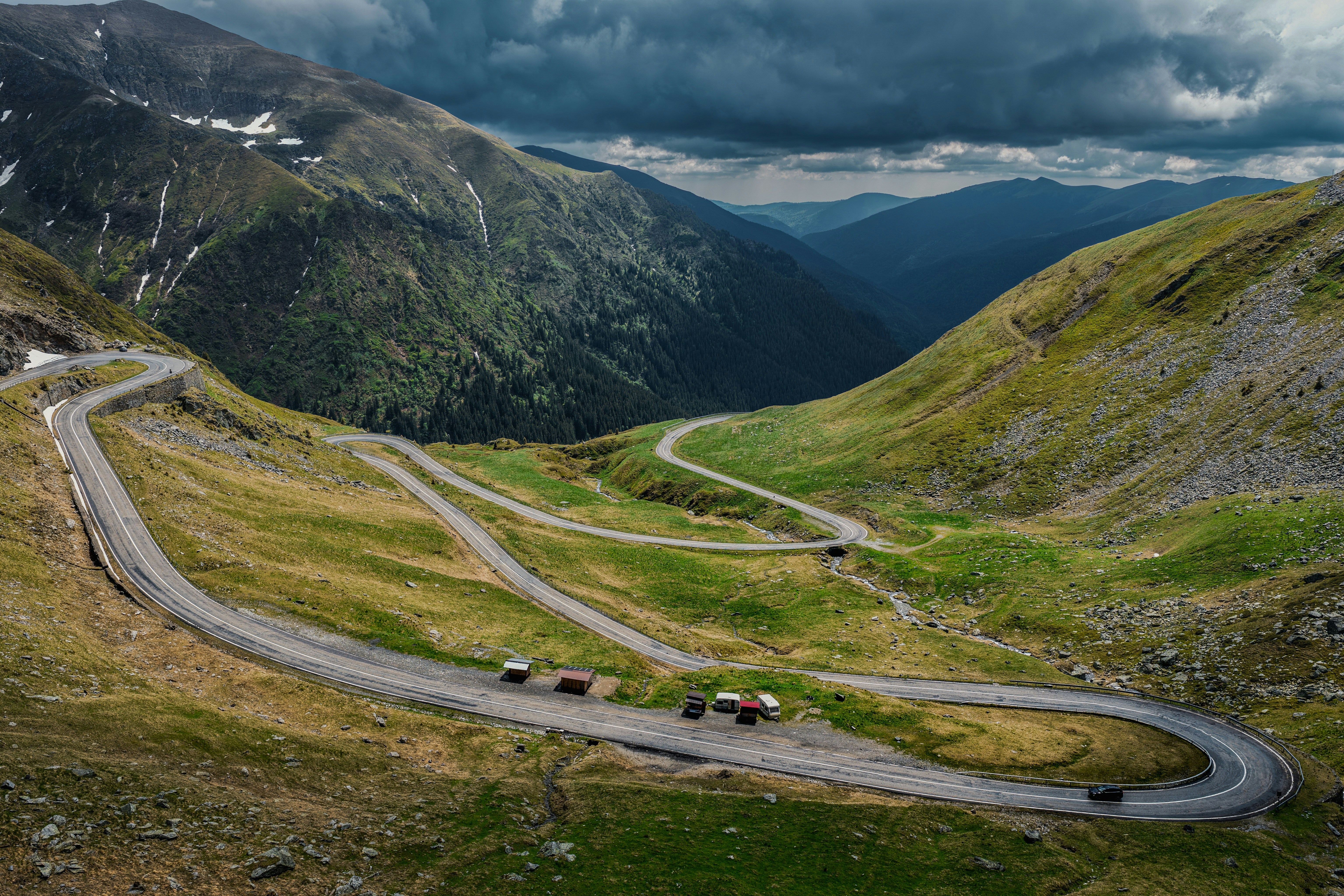 A winding mountain road with sharp switchbacks through a green valley under dark clouds