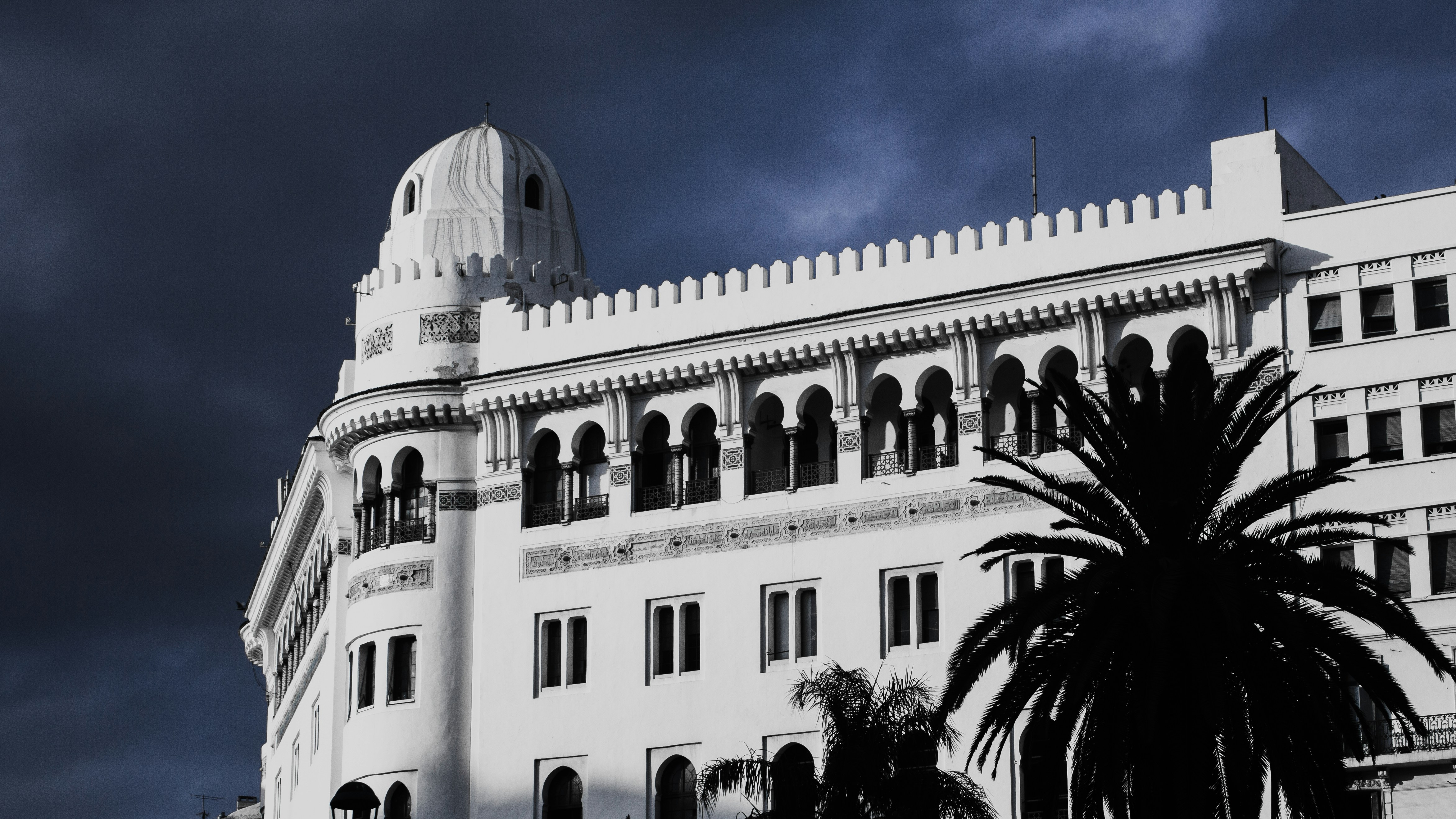 A white building with arched windows and a dome under a dark cloudy sky