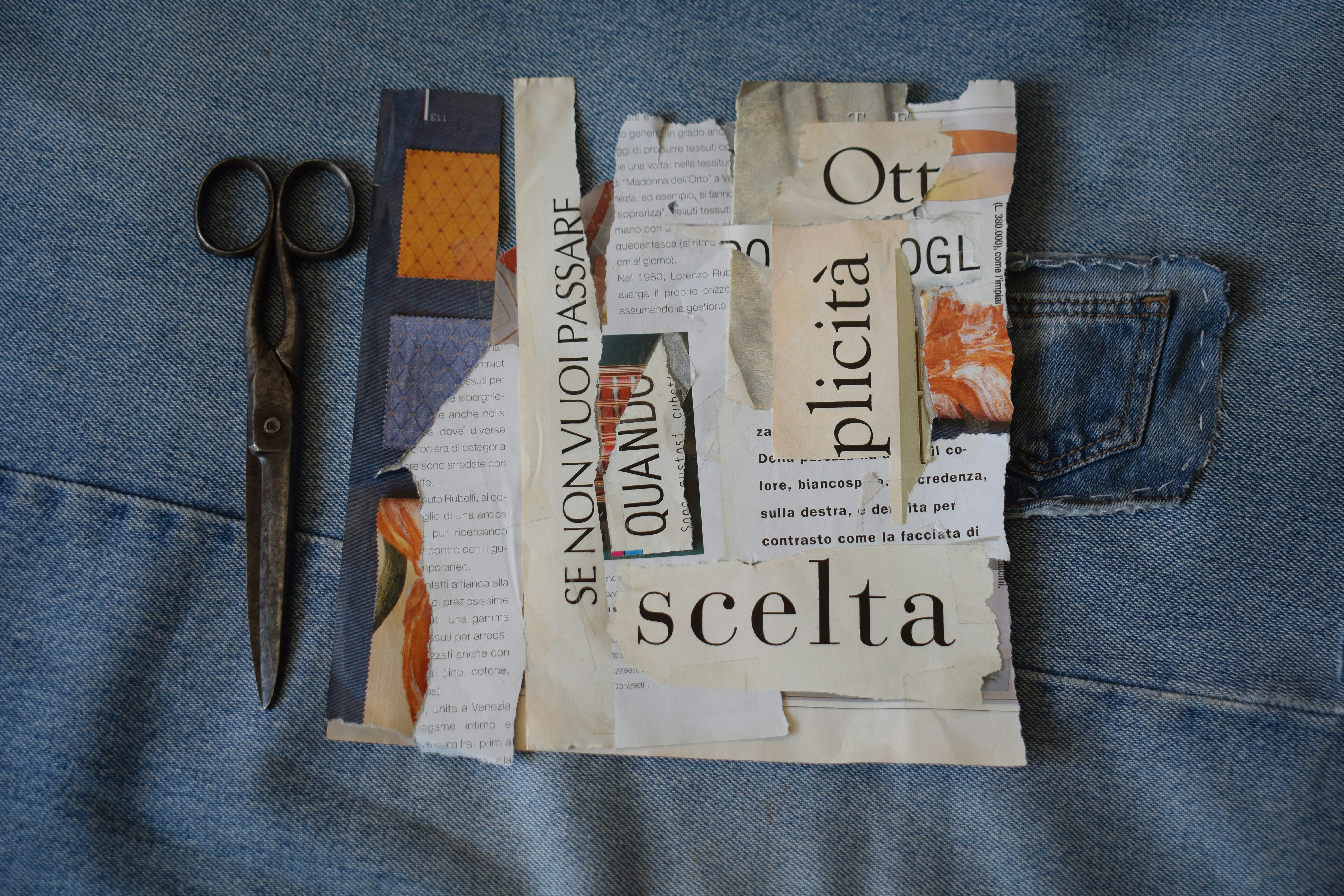 Vintage metal scissors beside a collage of torn paper scraps on blue denim fabric
