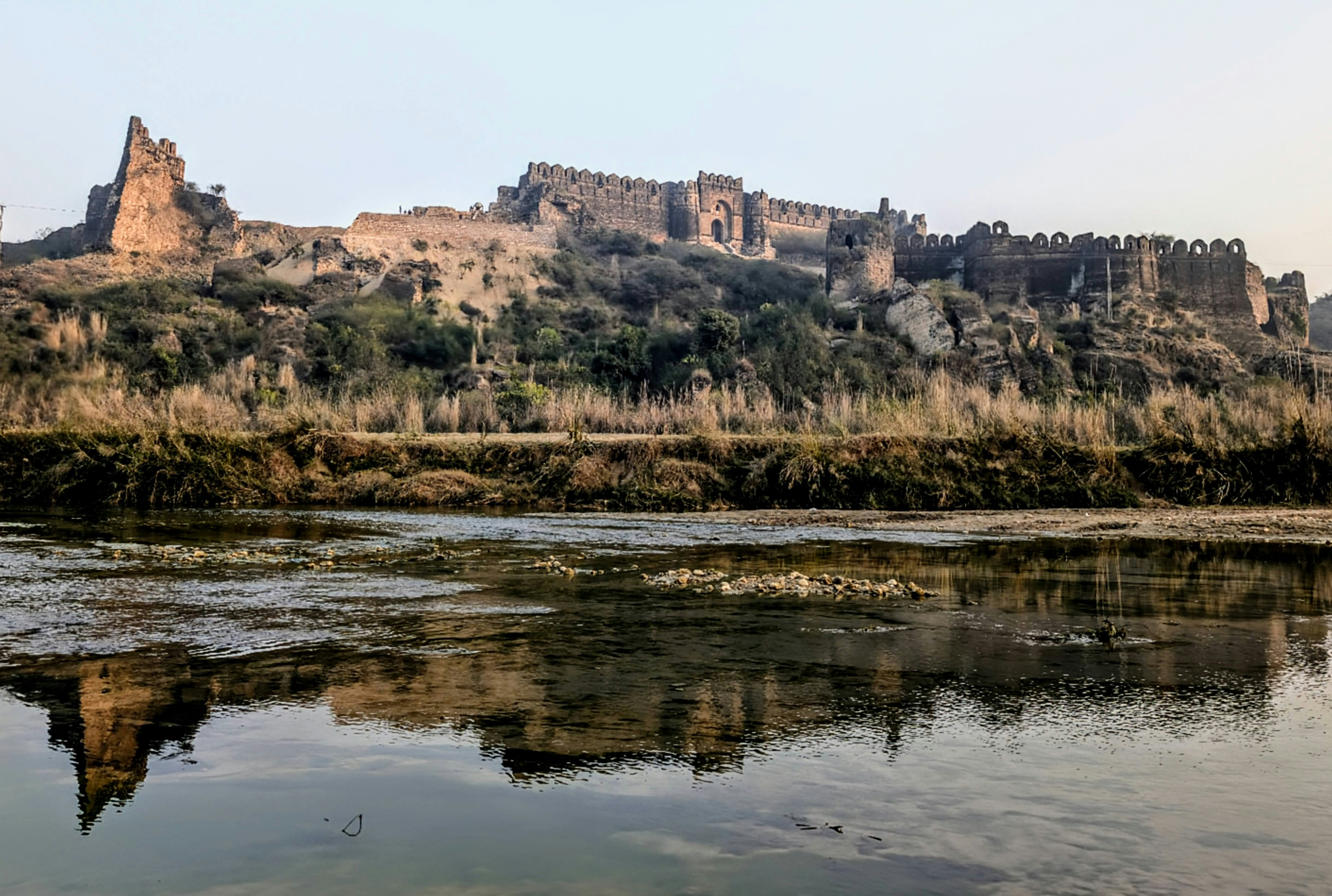 An ancient stone fortress on a hill reflecting in a calm river