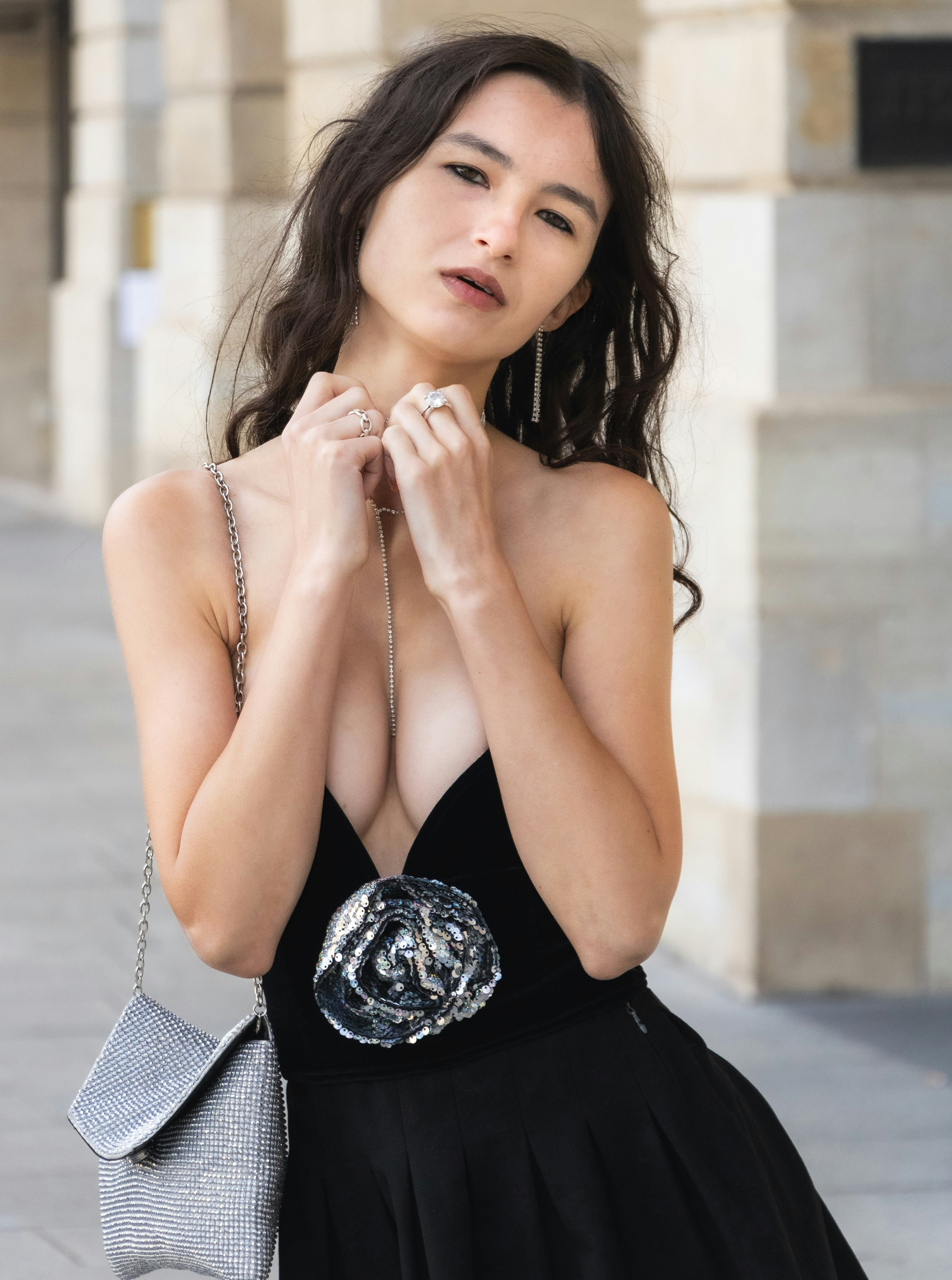 A woman in a black dress with a sequined rose detail and silver handbag