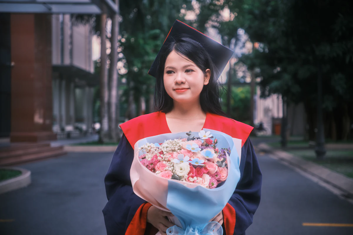 Wisudawati mengenakan toga sambil memegang buket bunga