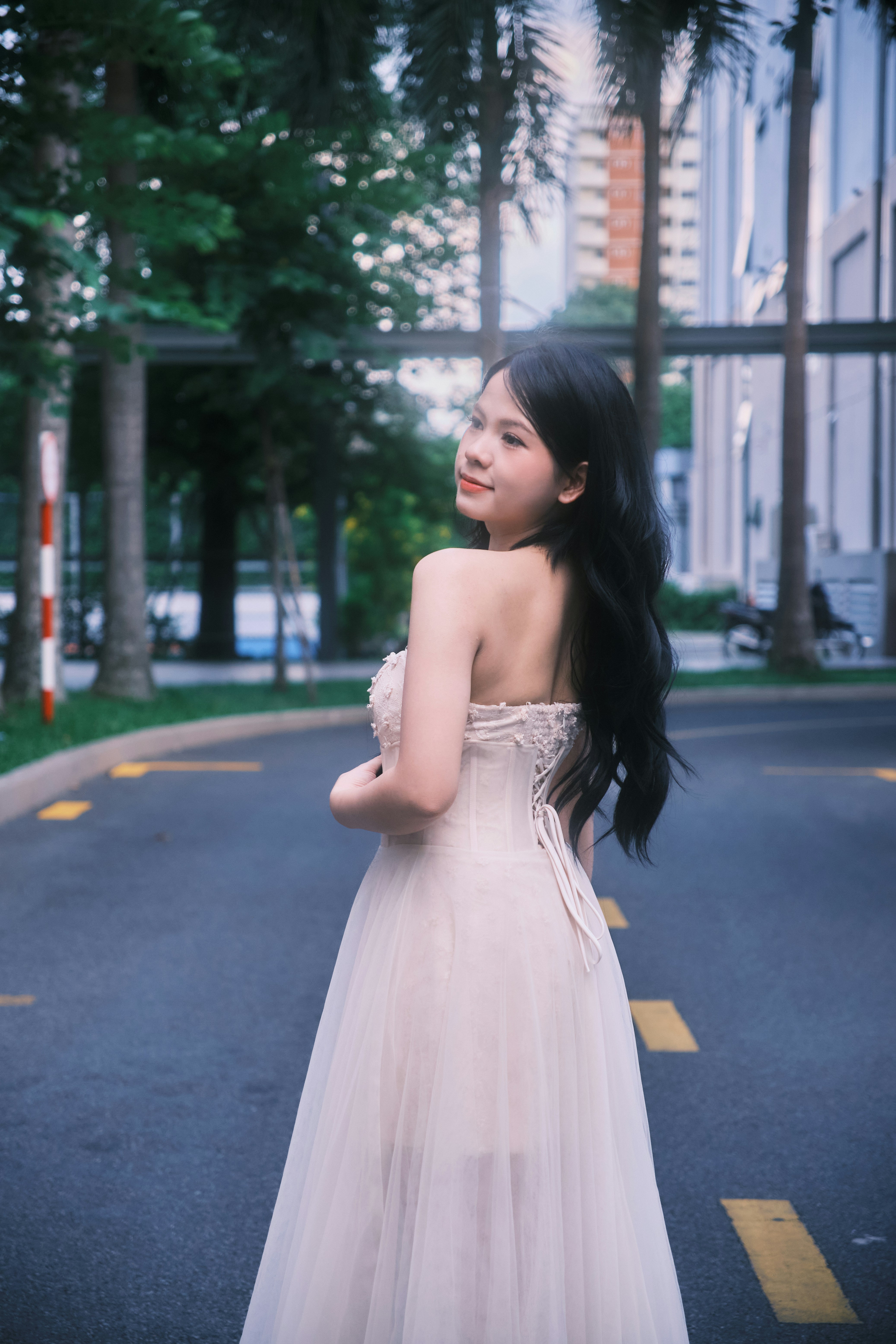 A woman in a strapless white dress looking back on an asphalt road