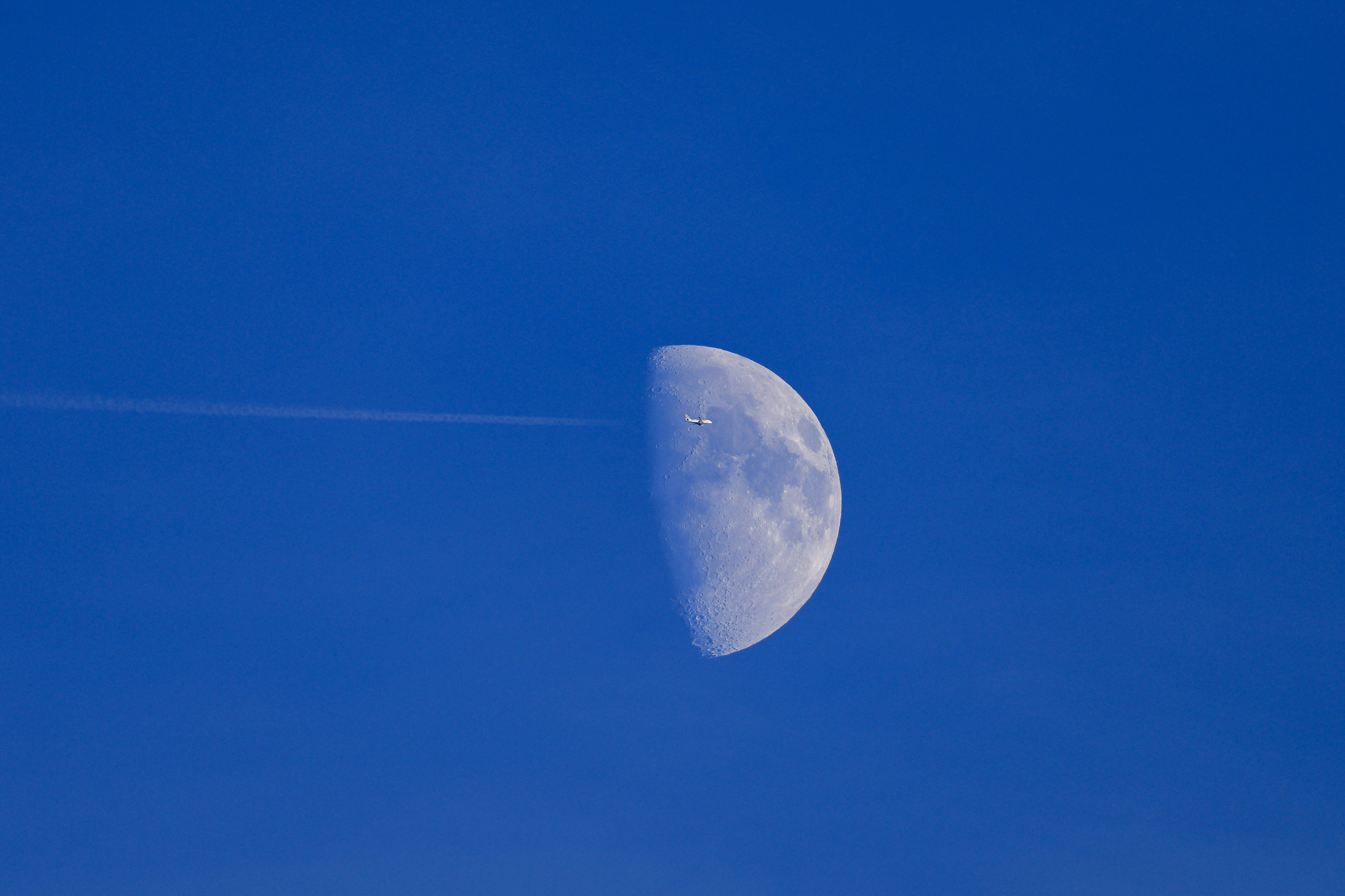 Un petit avion survolant une demi-lune dans un ciel bleu clair