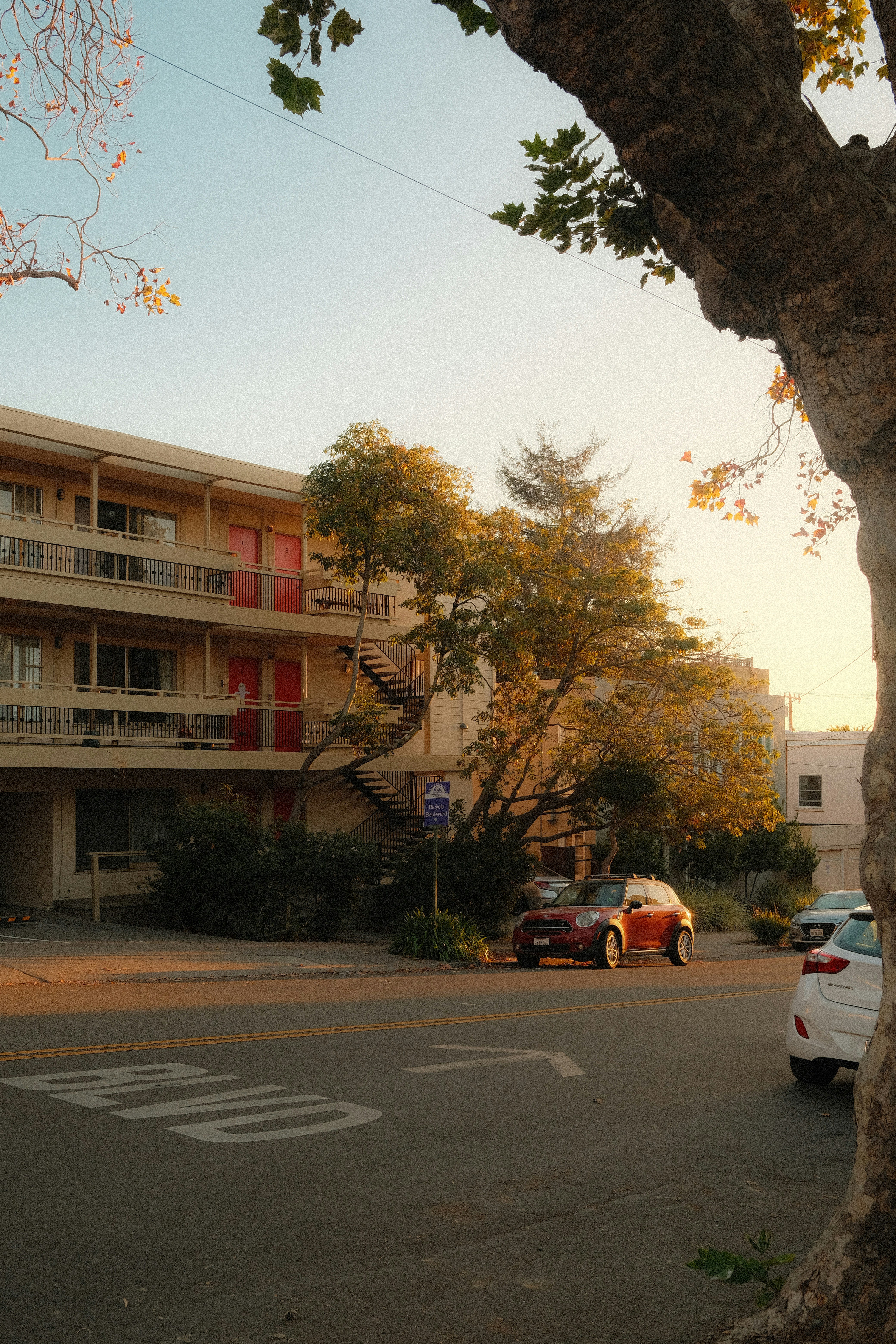 A red car parked on a street beside a multi-story apartment building