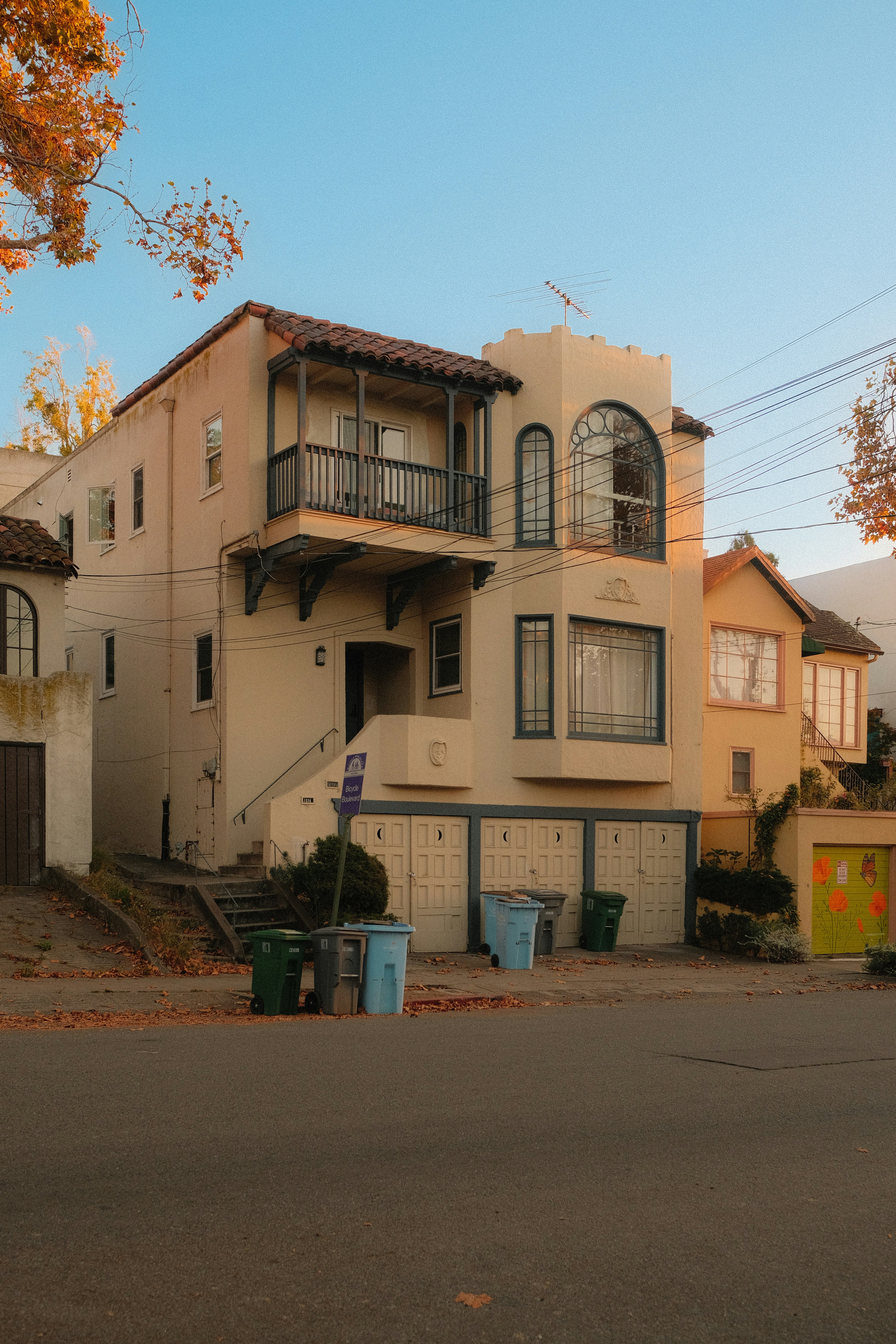 A multi-story stucco house with a balcony and garage doors on a quiet street