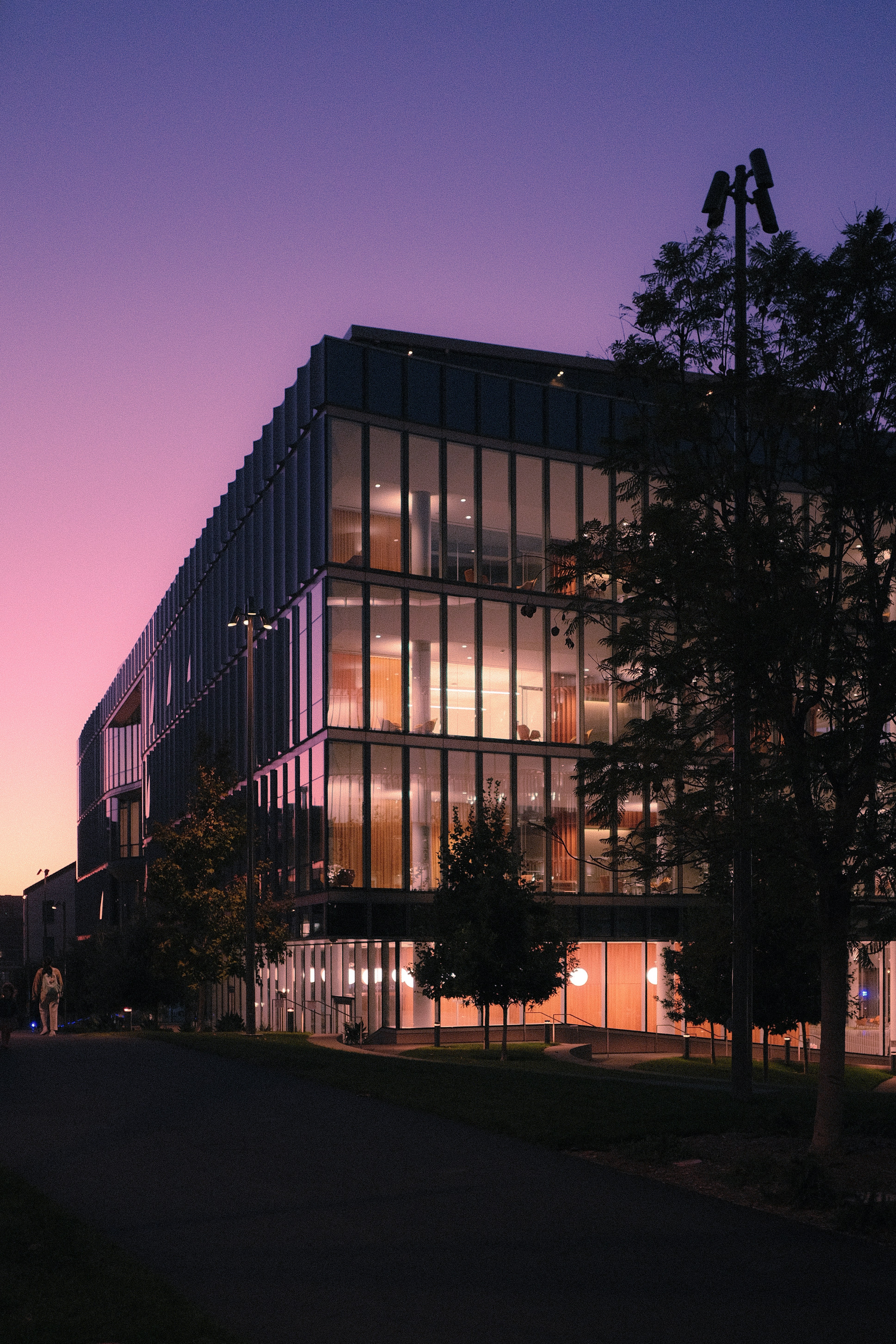 A modern glass office building illuminated at night under a purple gradient sky