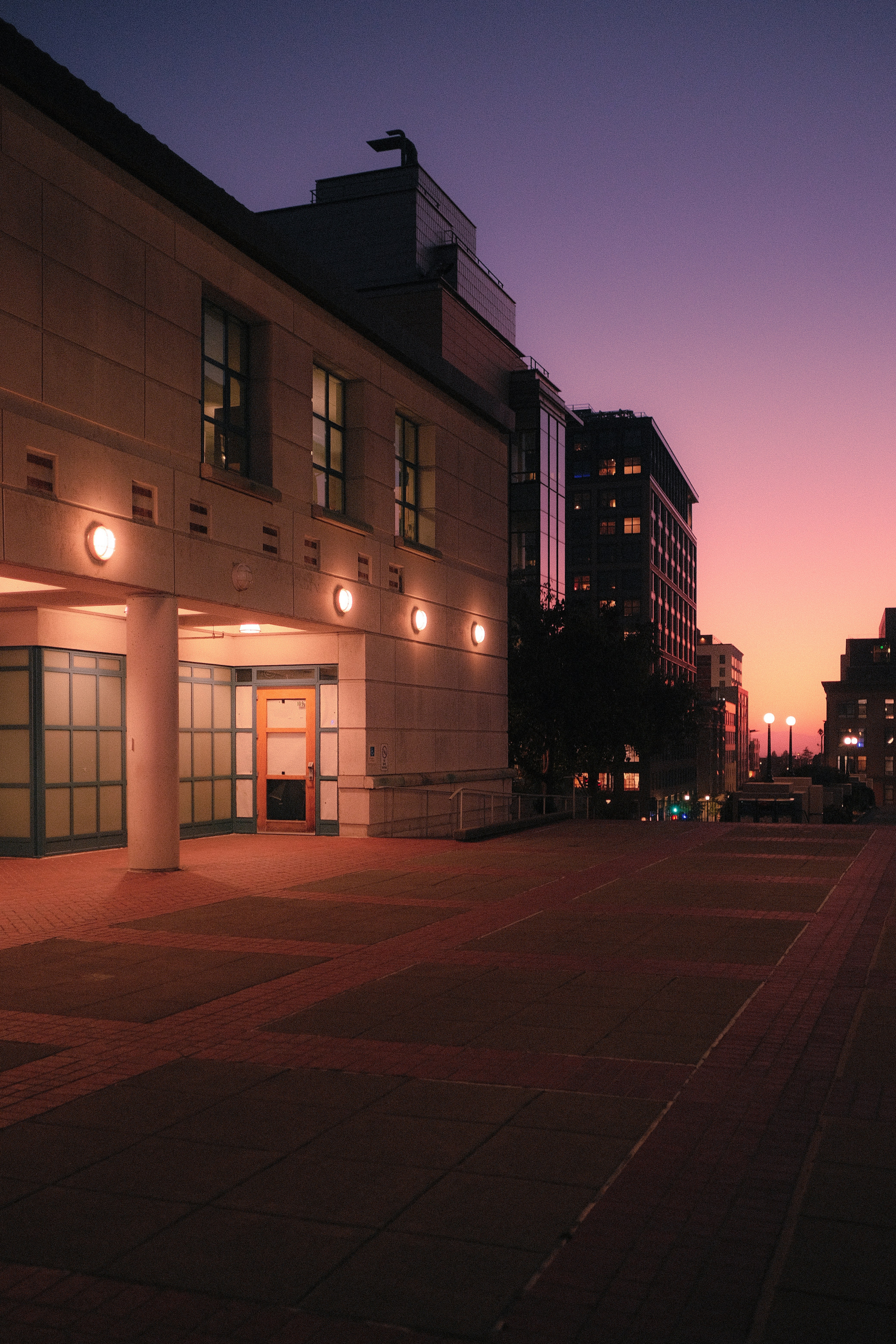 A modern building entrance with warm wall lights at a purple gradient sky