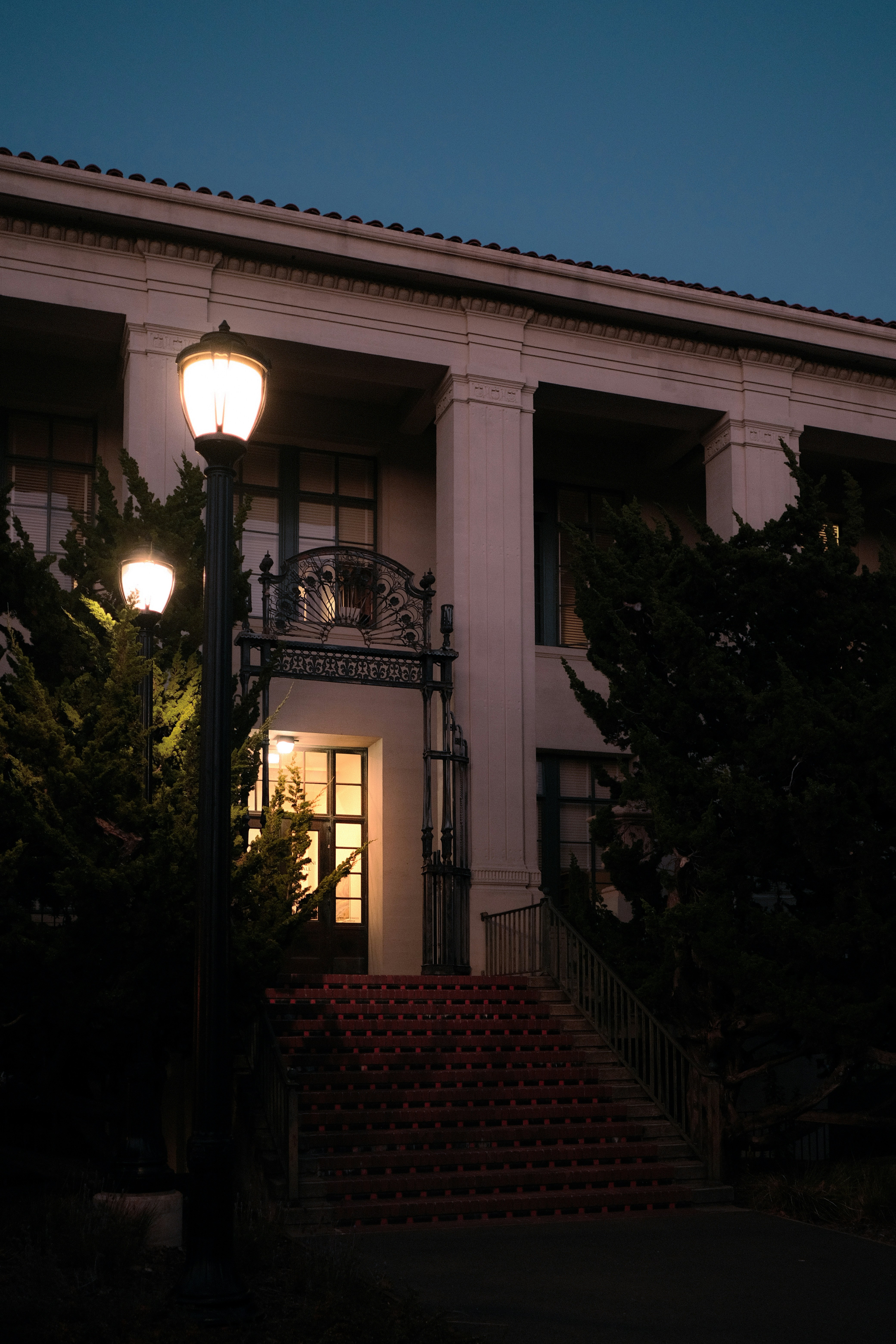 A building entrance with stone stairs and glowing lamps at night