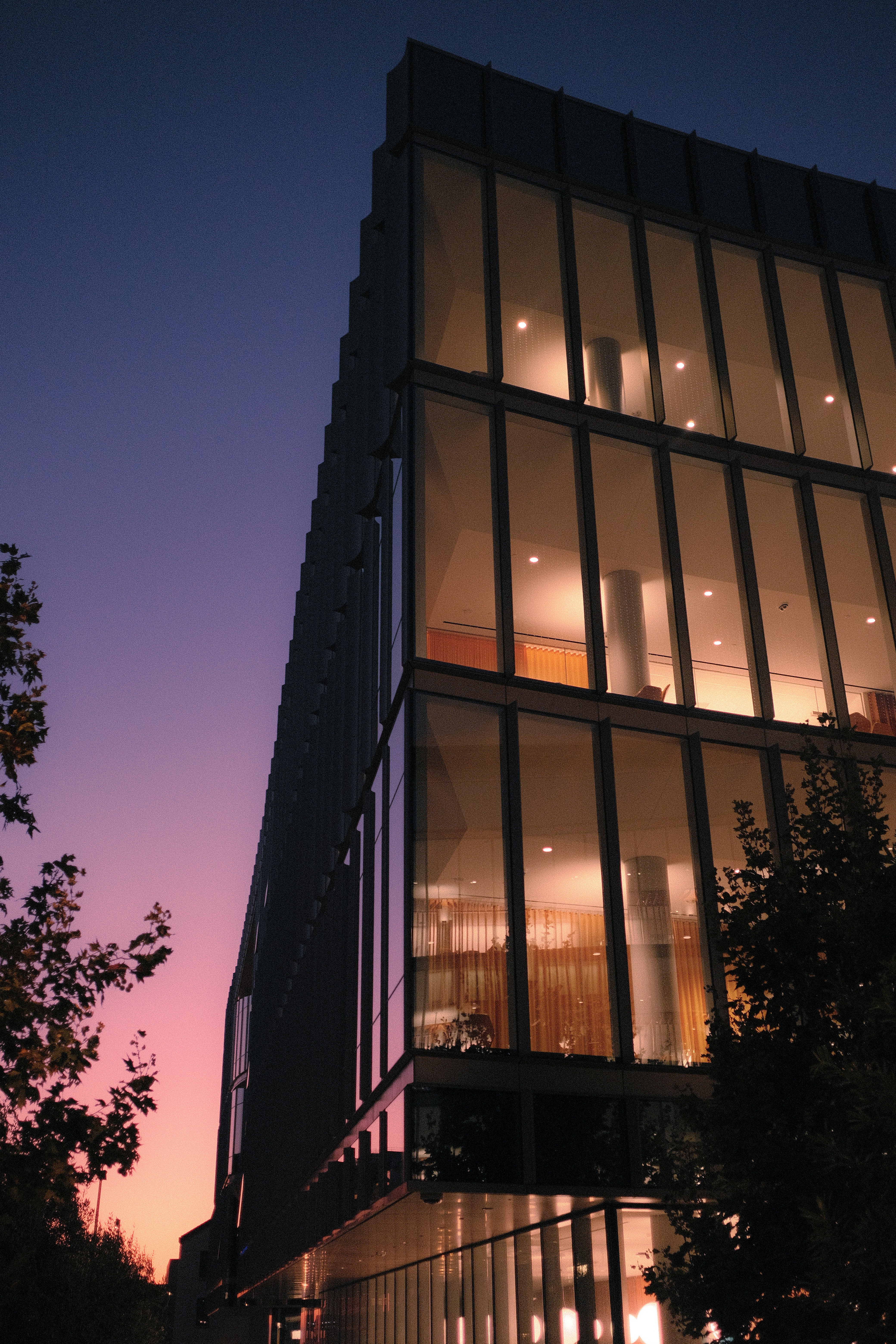 A modern glass office building against a purple and orange gradient sky
