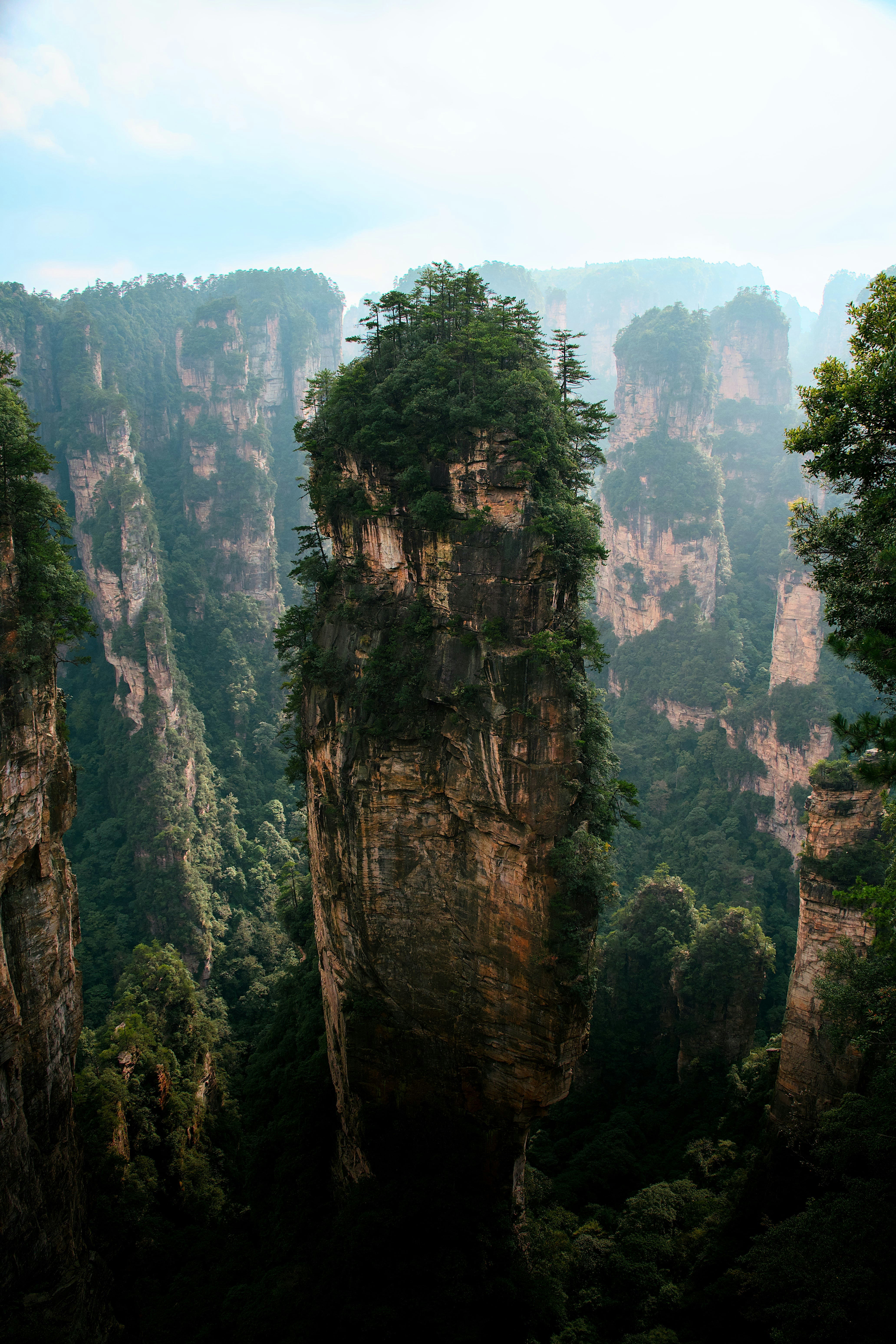 A tall sandstone pillar topped with green trees in Zhangjiajie National Forest Park