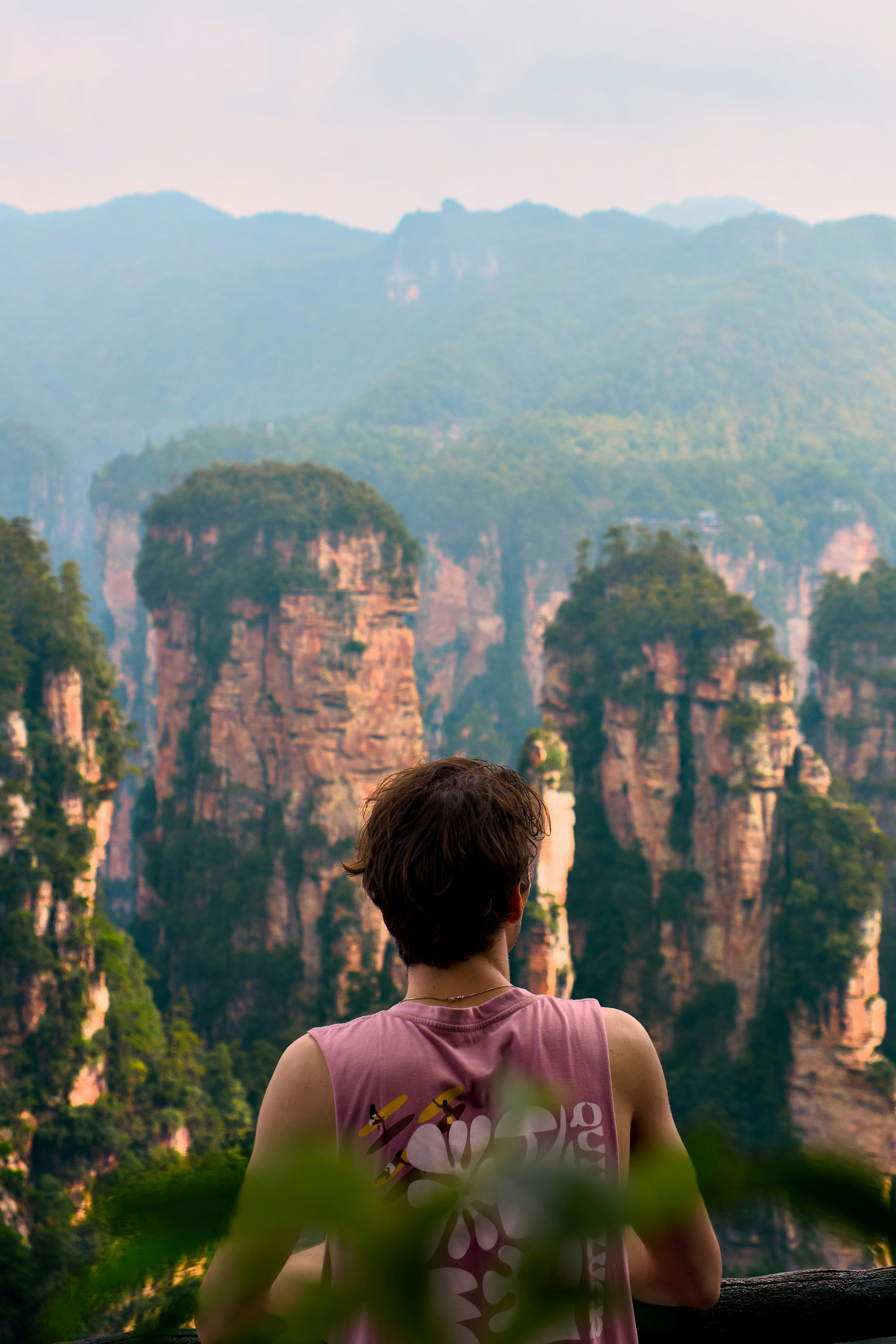 Una persona con una camiseta de tirantes rosa mirando imponentes pilares de arenisca en Zhangjiajie