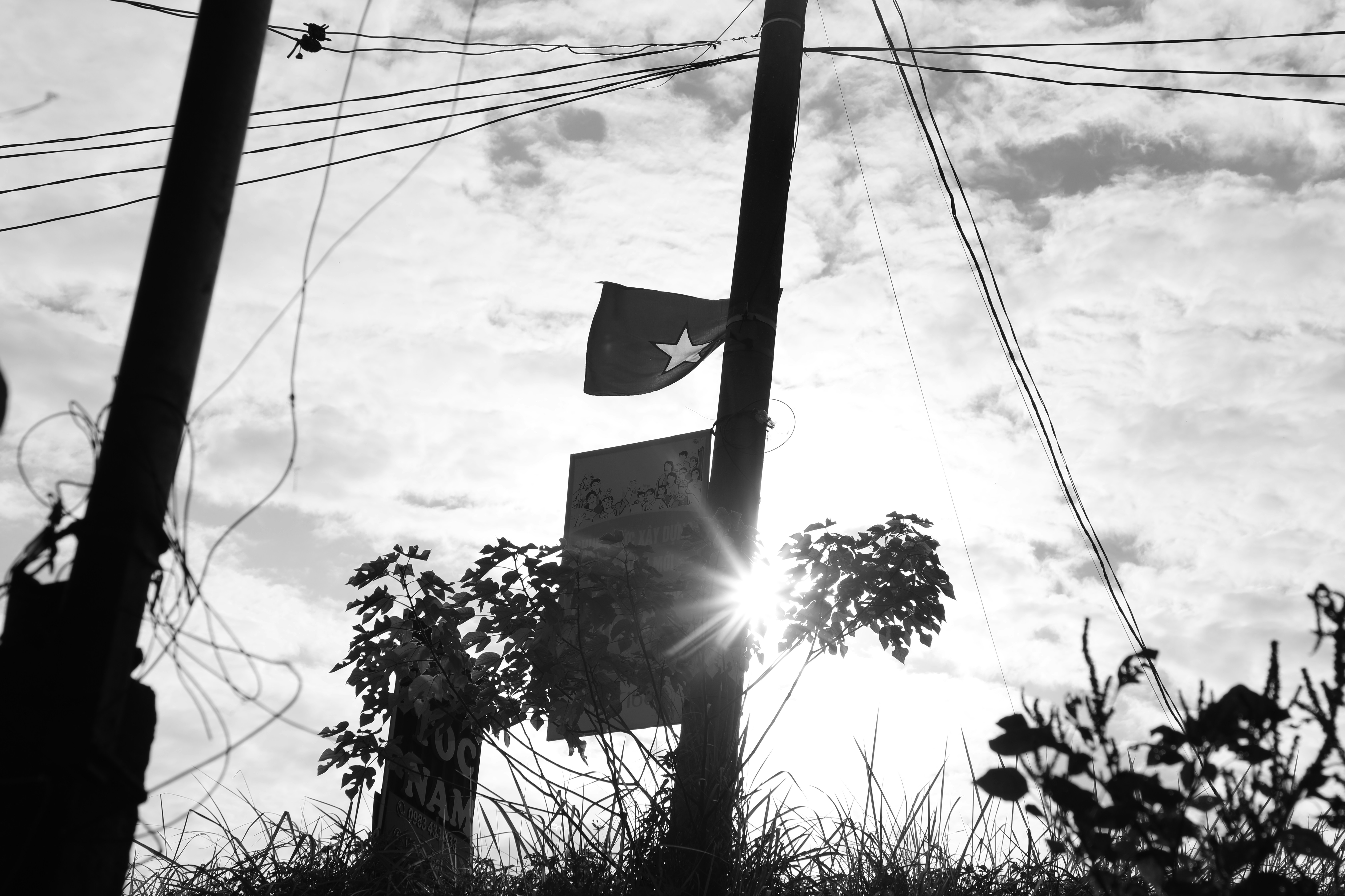 A flag with a star on a utility pole against a bright sunlit sky