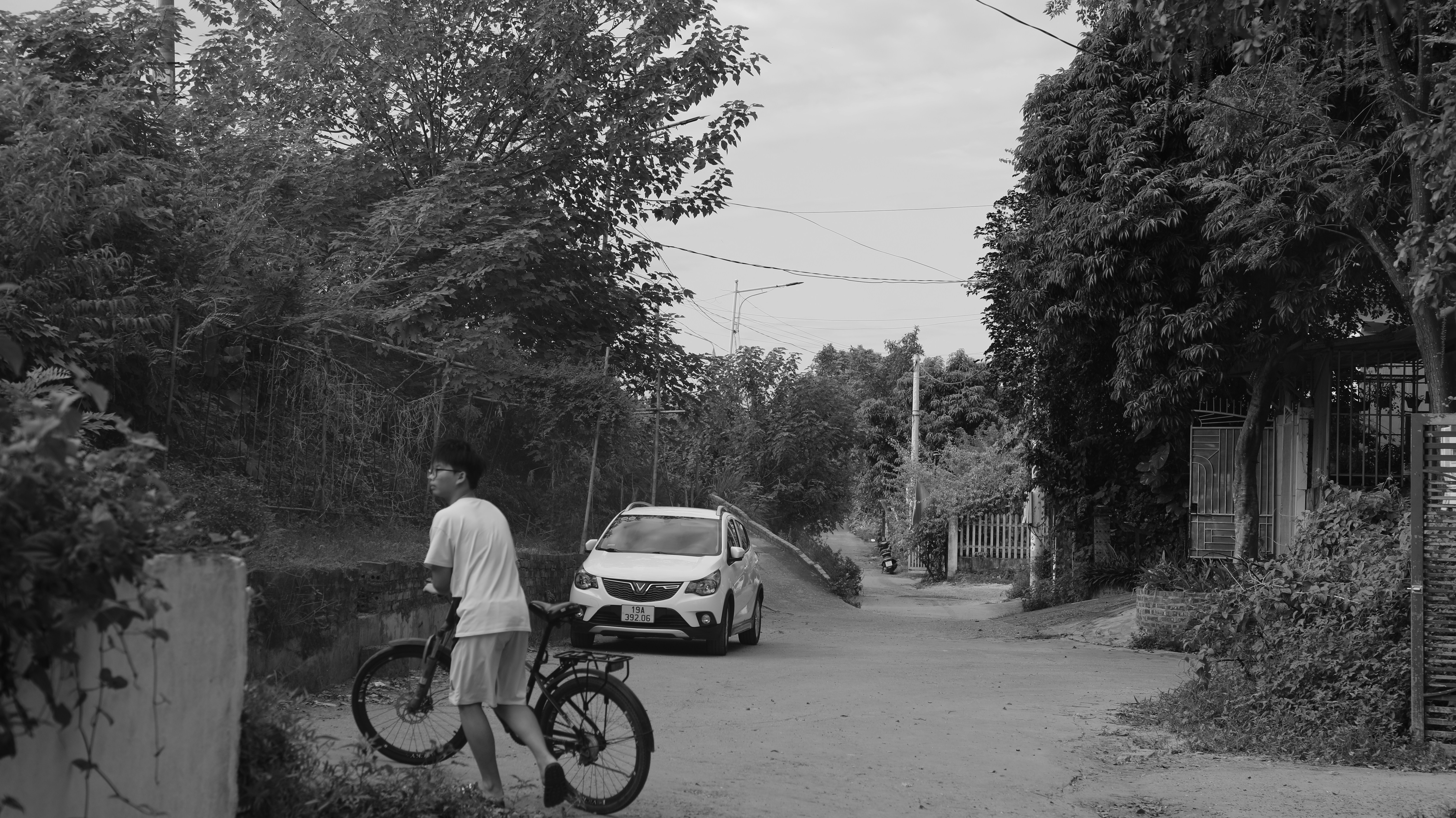 A person walking a bicycle along a quiet road with a white car