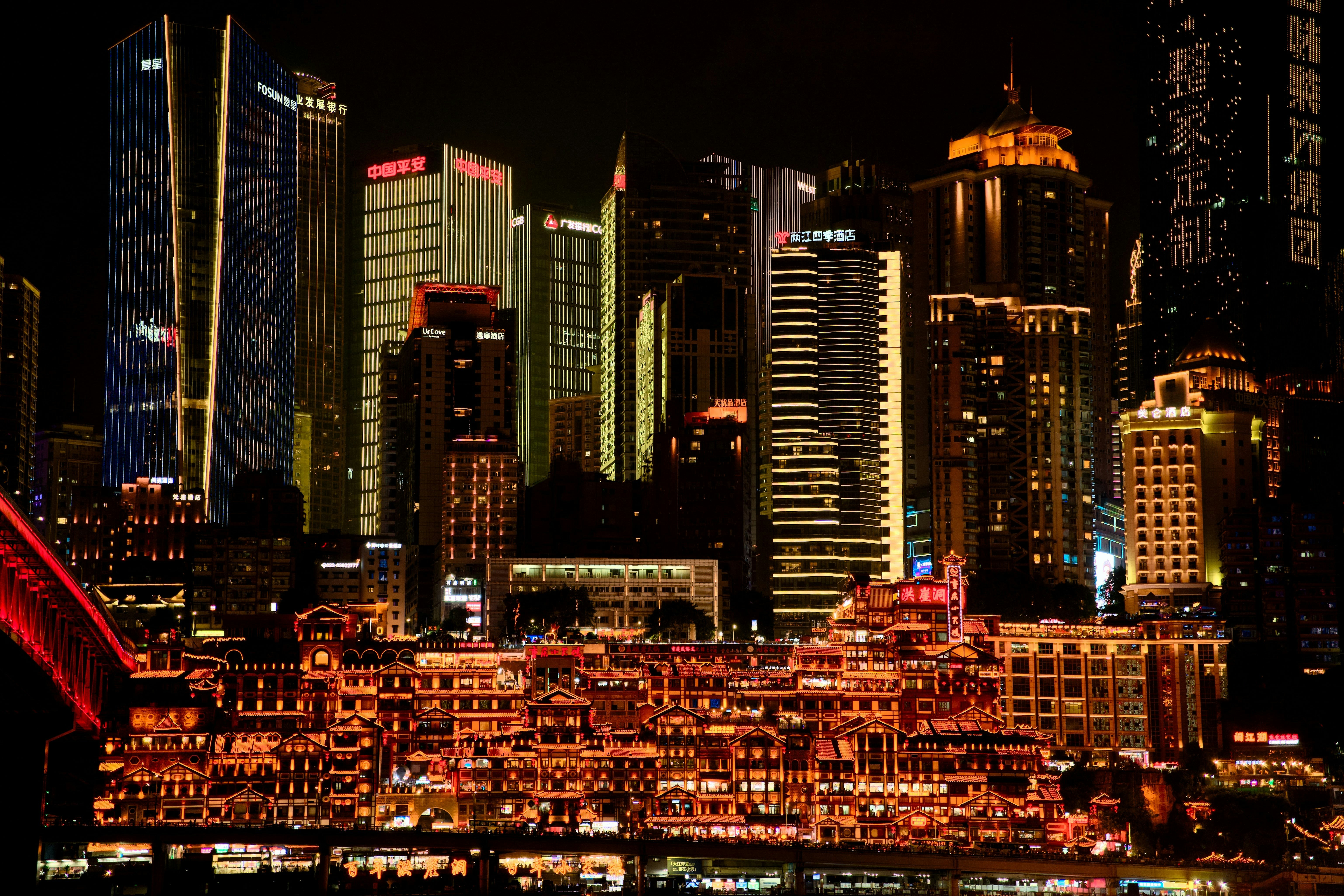 Edificios tradicionales iluminados bajo rascacielos modernos en Chongqing por la noche