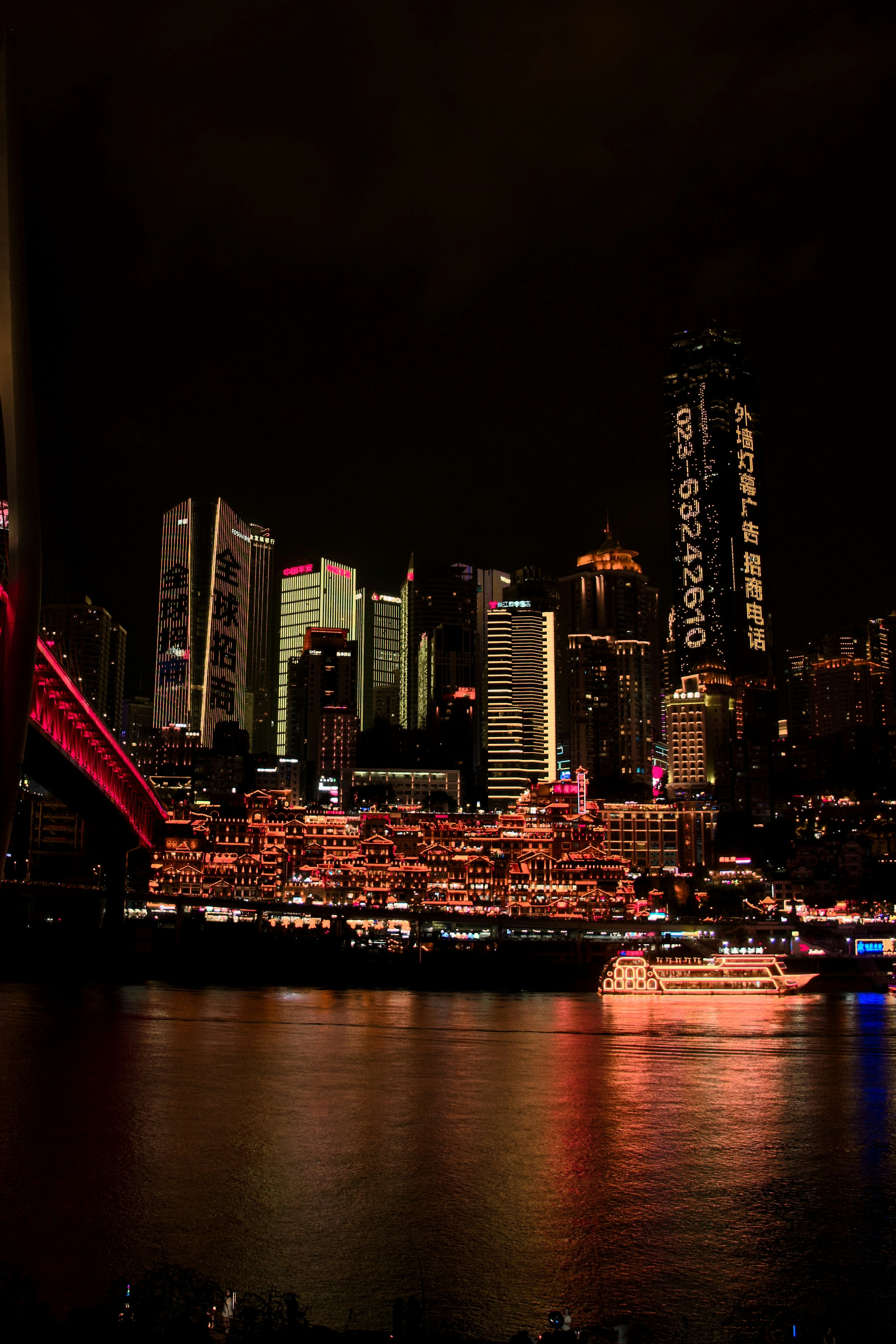 Illuminated skyscrapers and traditional buildings along a river at night in Chongqing