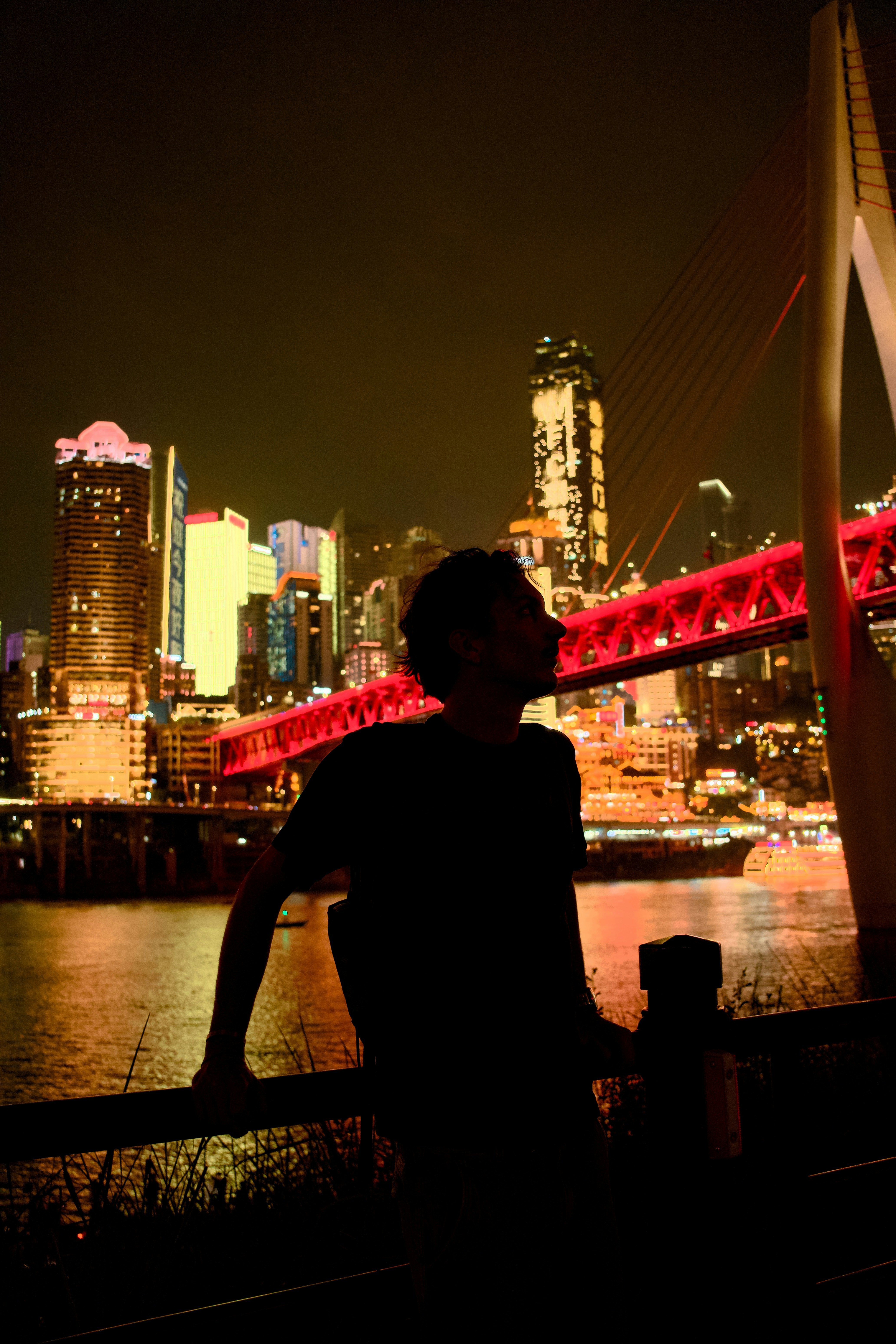 A person in silhouette against a brightly lit city skyline and red bridge