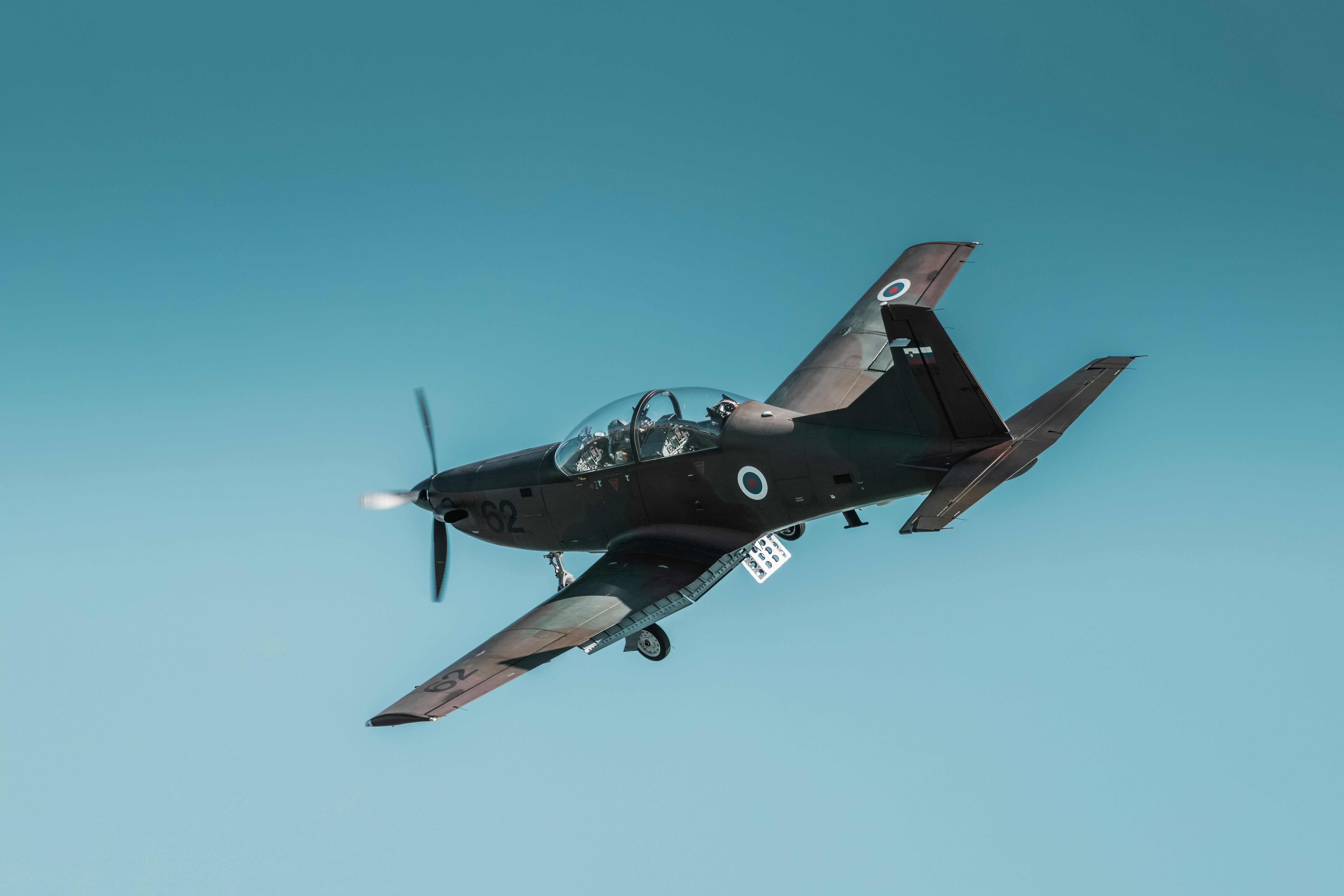 Pesawat latihan militer turboprop gelap yang berbelok melawan langit biru cerah