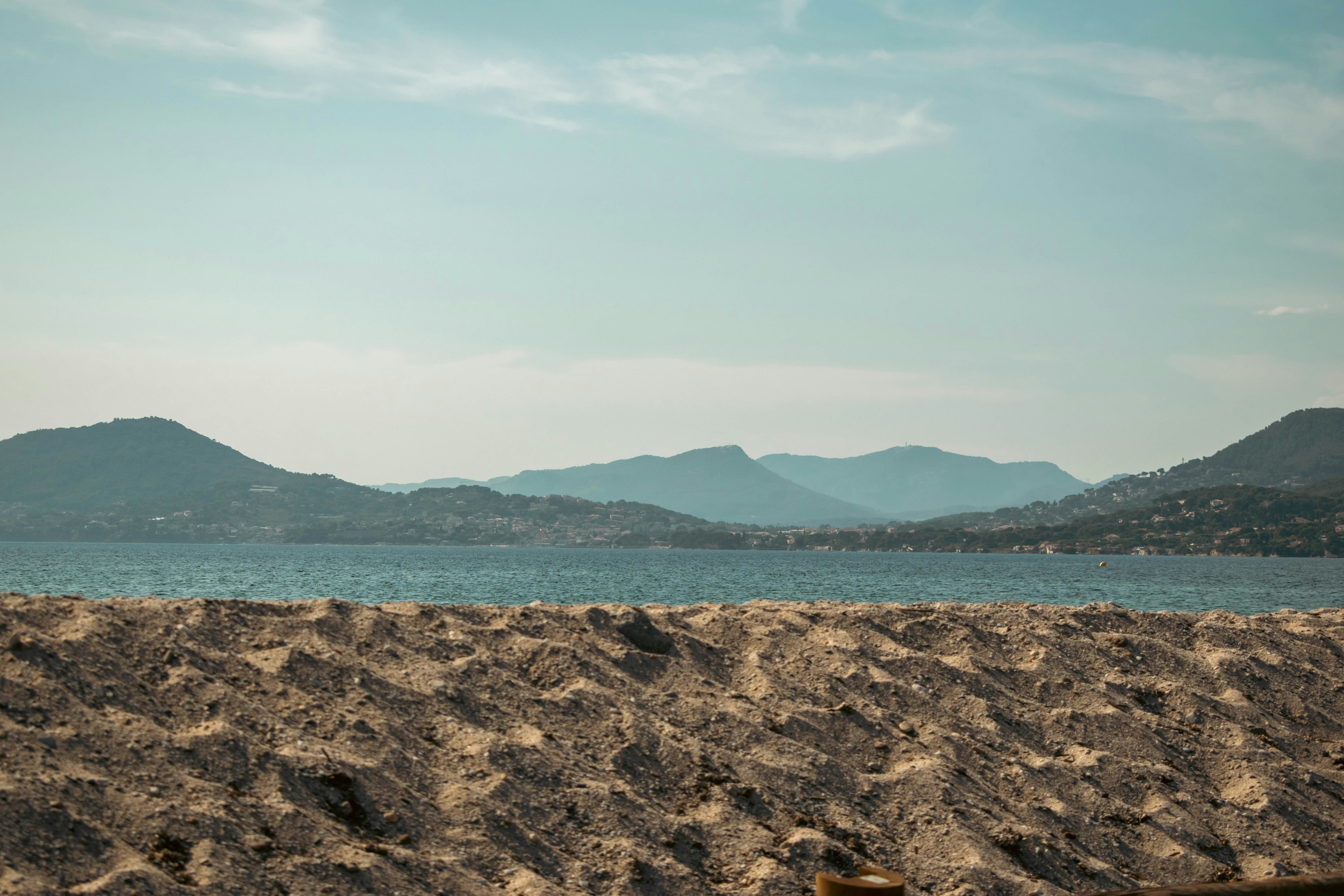 A sandy beach in the foreground with mountains across a calm blue sea