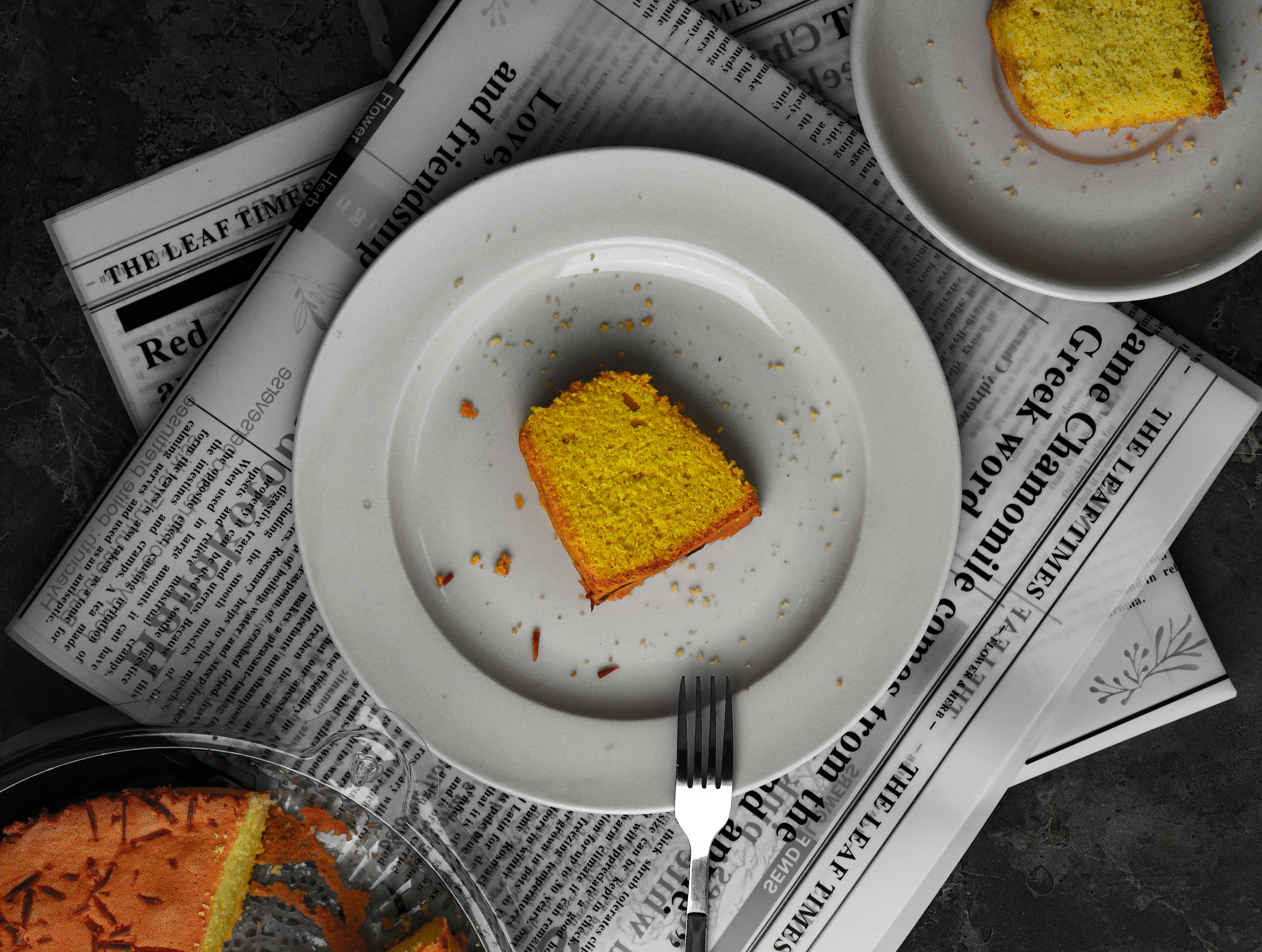 A slice of yellow cake on a white plate atop a newspaper
