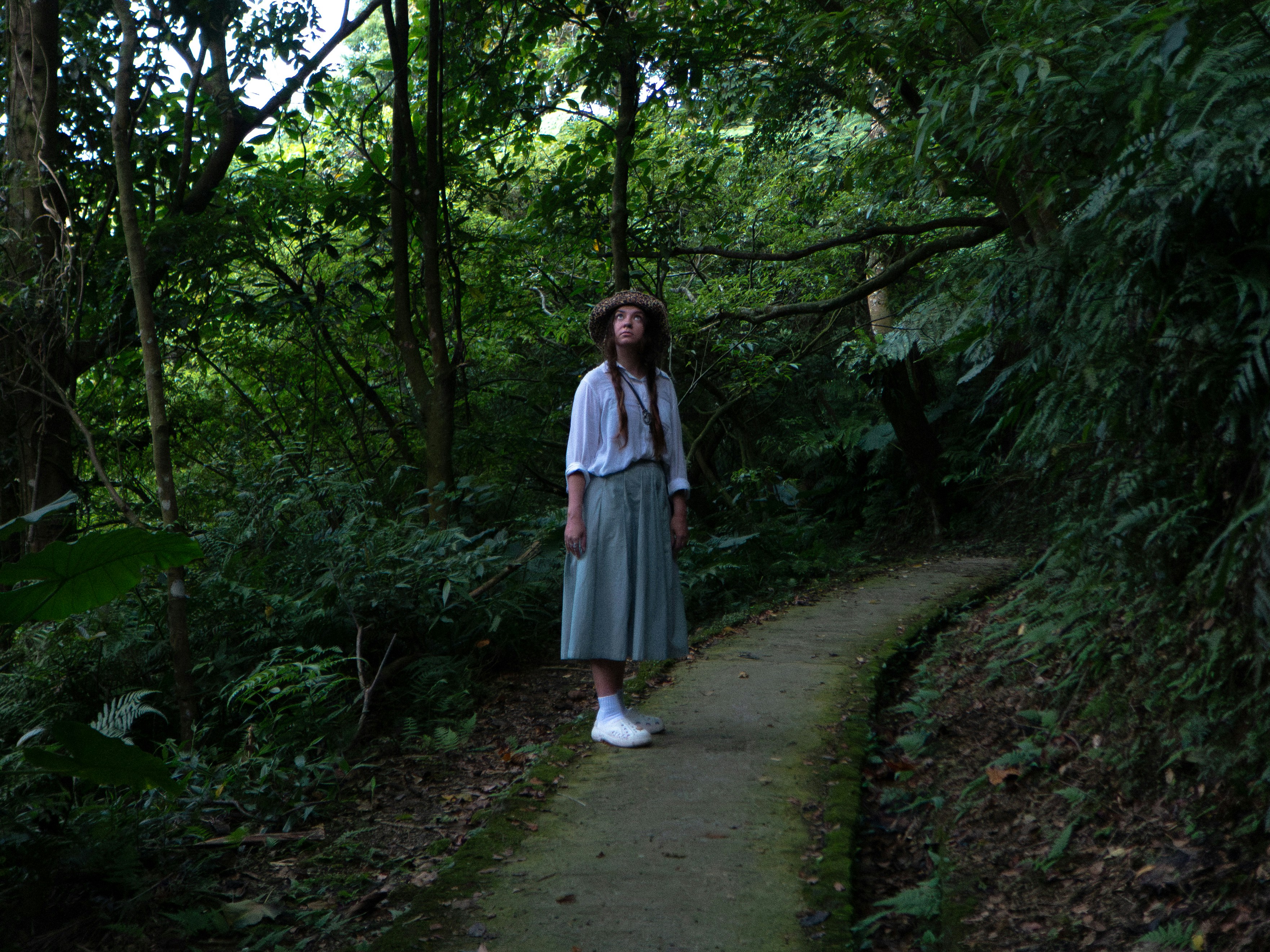 A woman in a white shirt and skirt on a mossy forest path