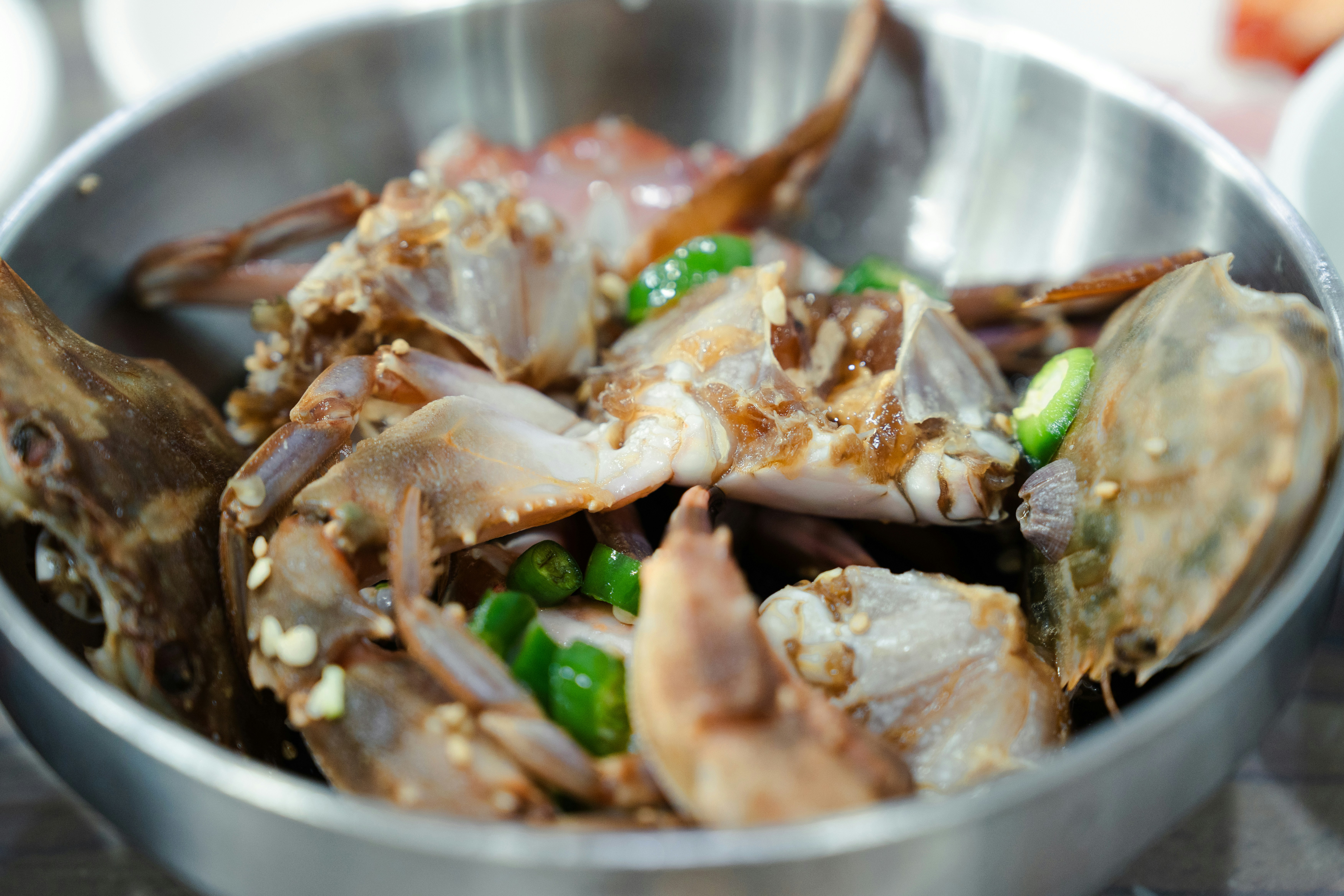 Marinated raw crab pieces with sliced green chili peppers in a metal bowl