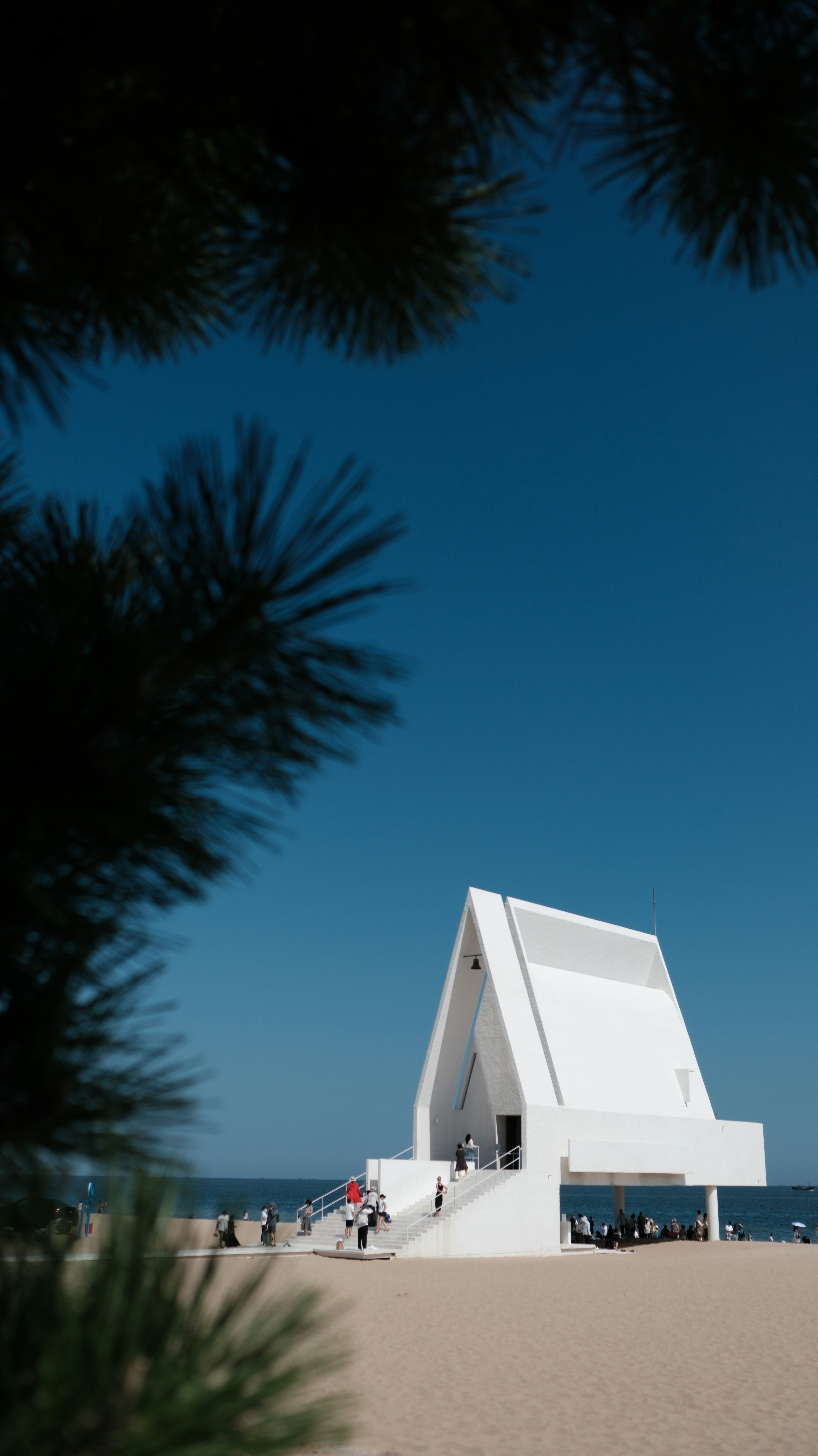 A white modern chapel on a sandy beach under a clear blue sky