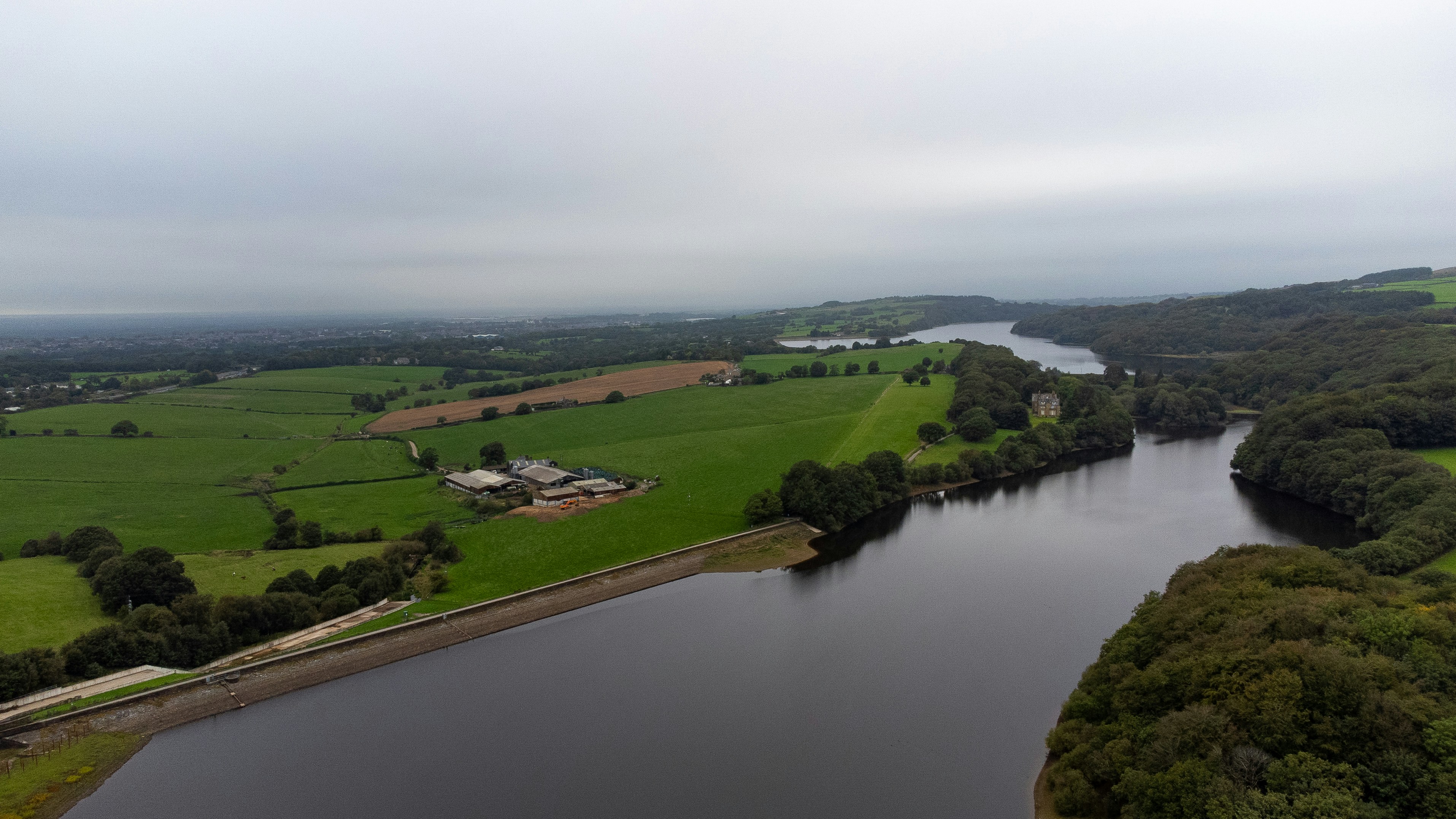An aerial view of a reservoir bordered by green fields and dense woodland