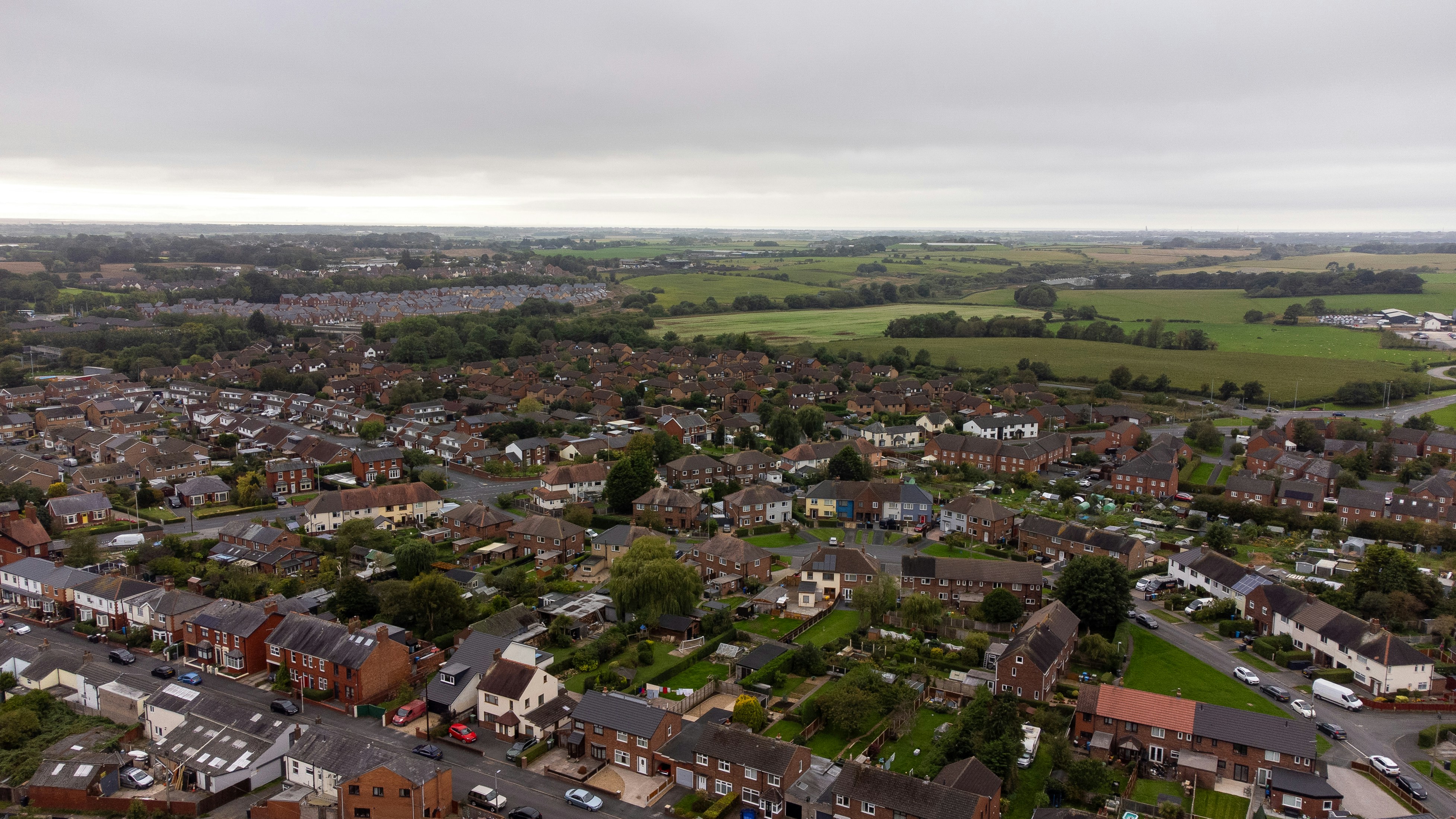 Aerial view of a suburban neighborhood with houses and green fields under cloudy skies