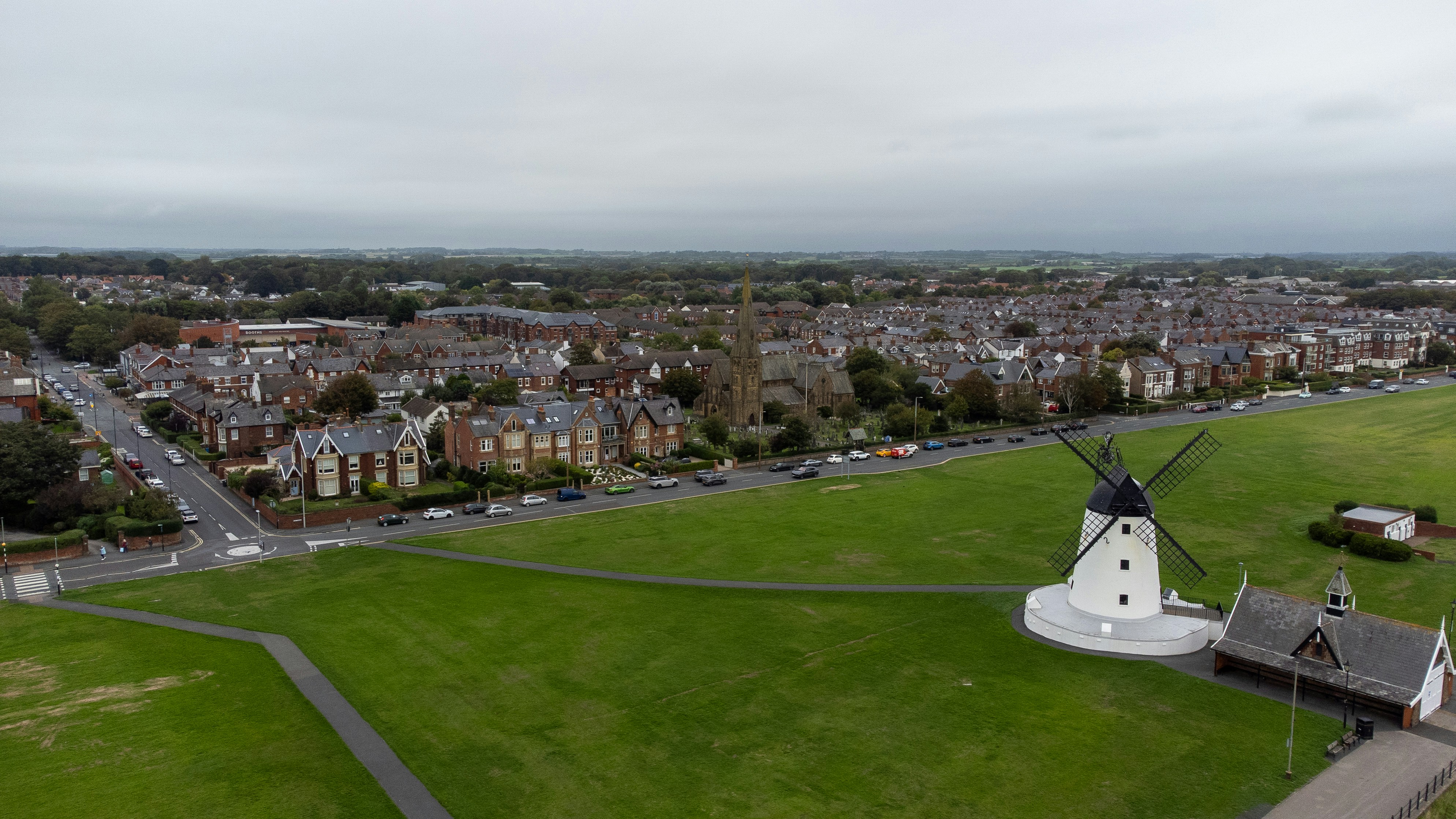 An aerial view of a white windmill beside a green park and town