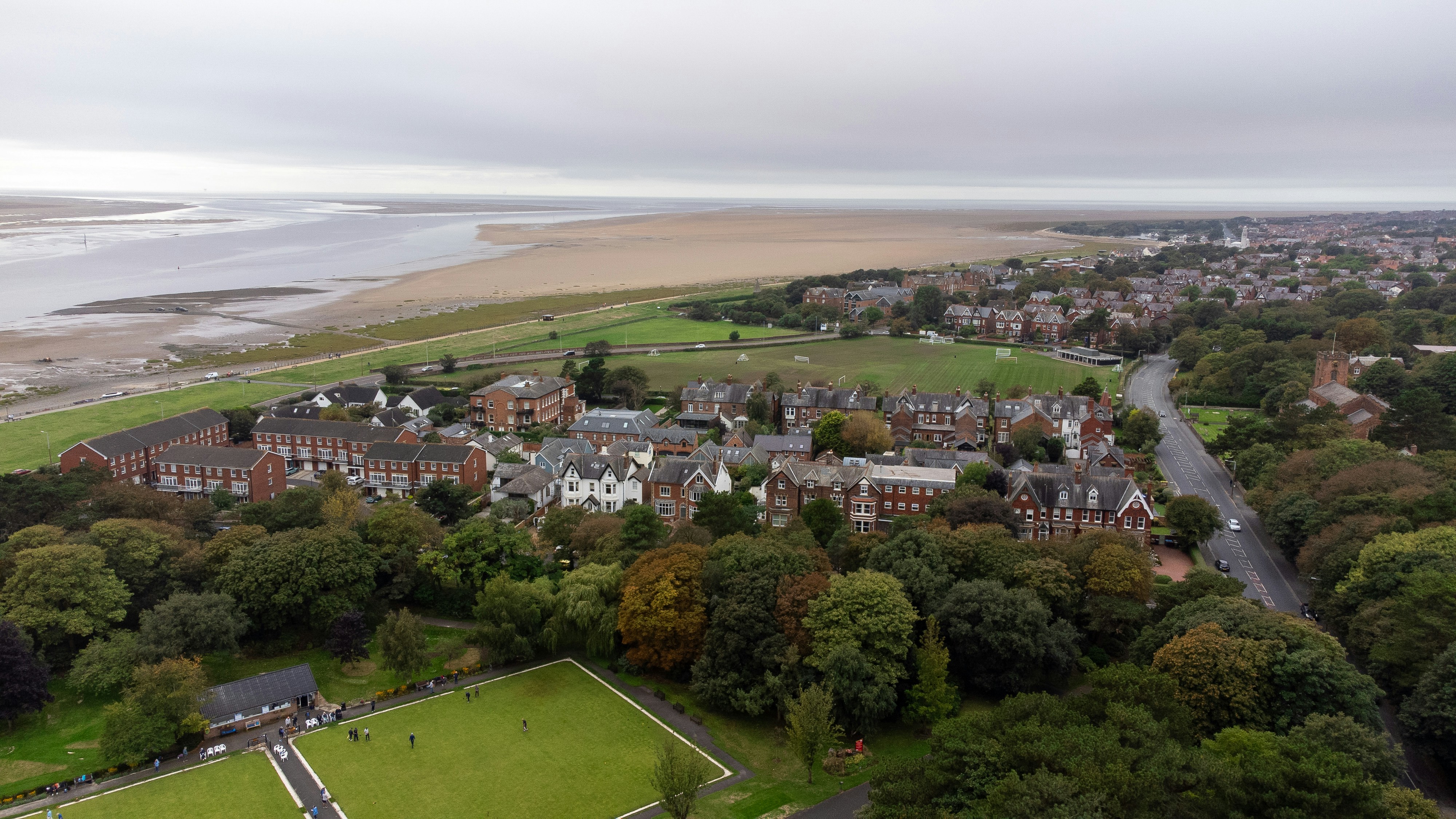 Aerial view of a coastal town with brick houses, green fields, and sandy beaches