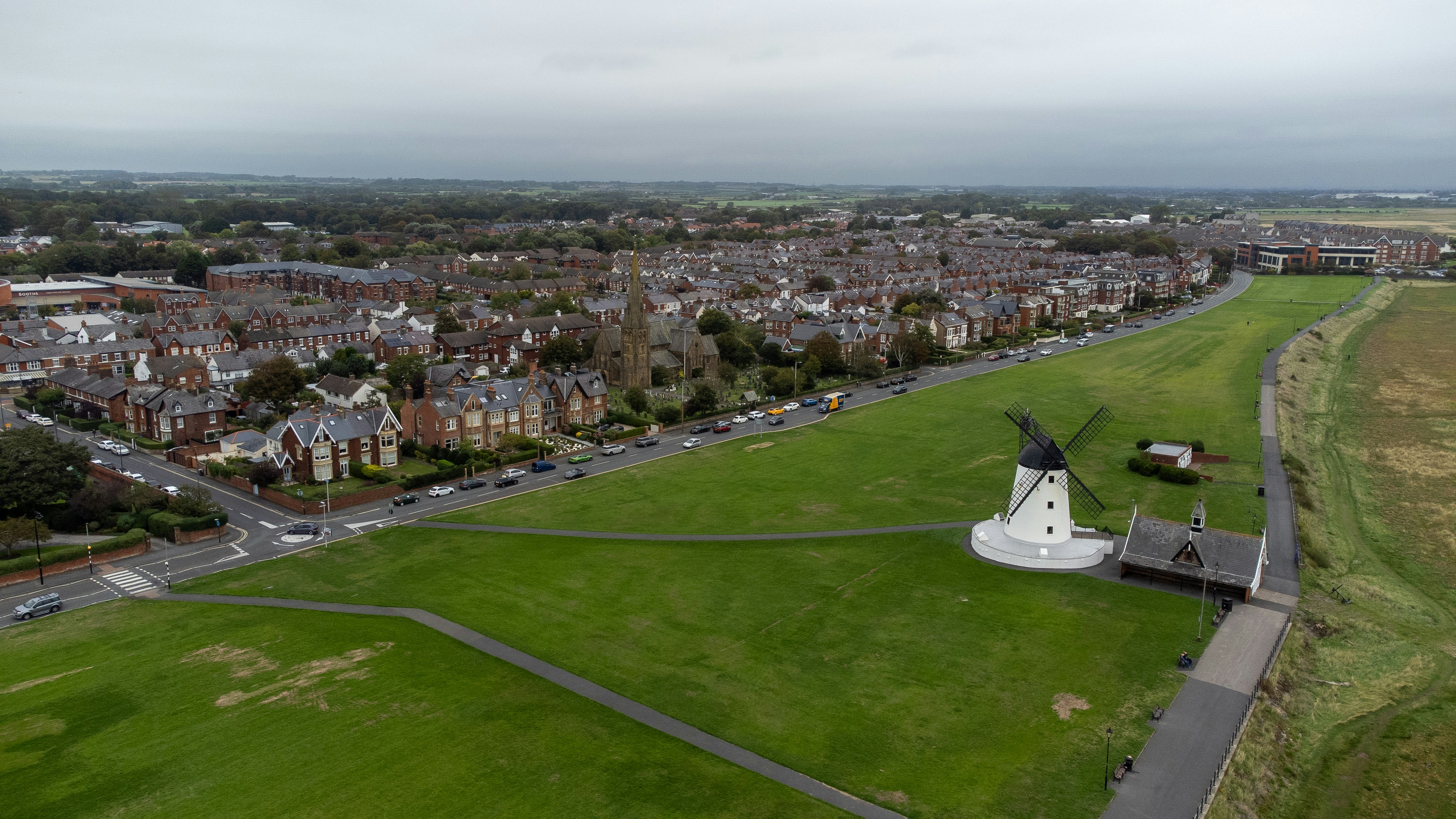 An aerial view of a white windmill on a green field beside a town