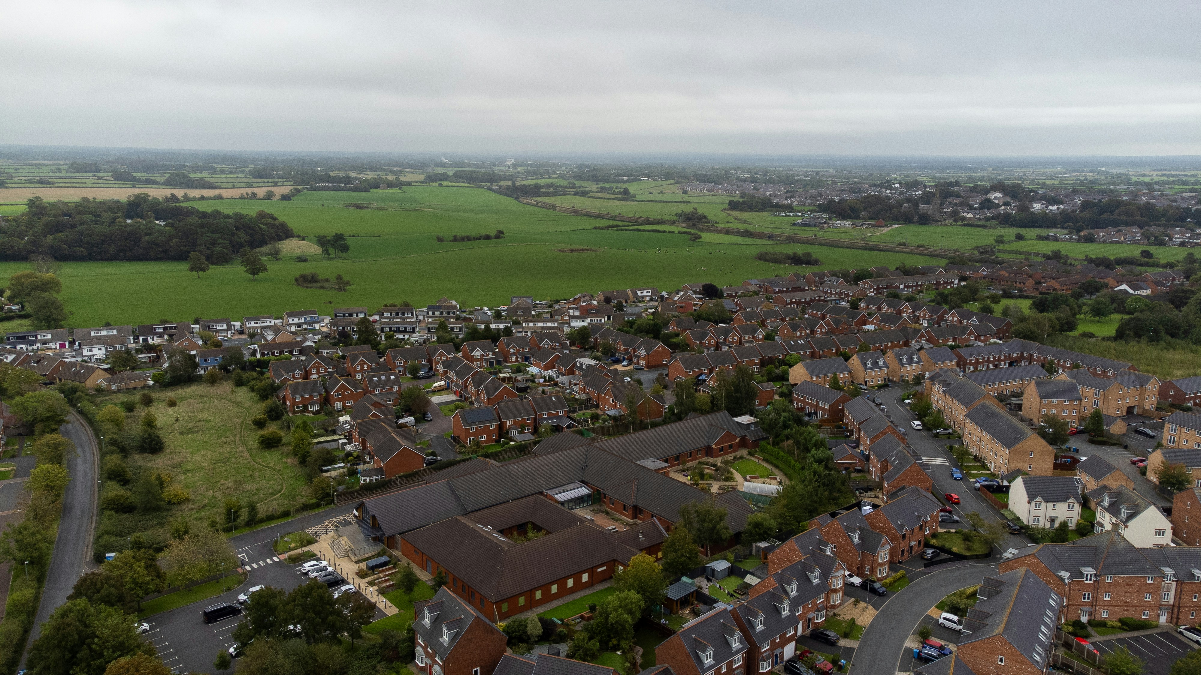 Aerial view of a residential neighborhood with brick houses bordering green fields