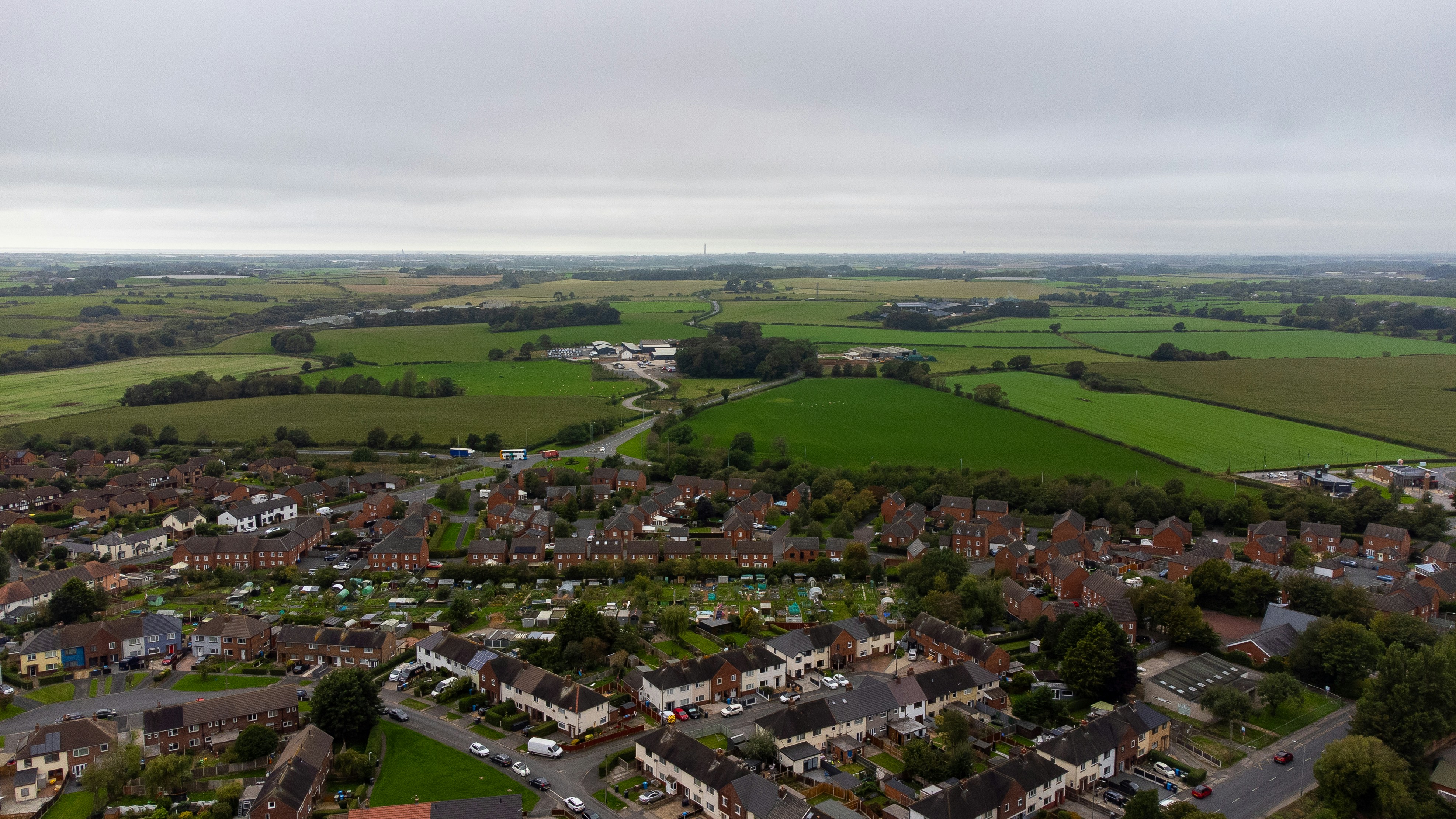 An aerial view of a residential neighborhood bordering green agricultural fields under a cloudy sky