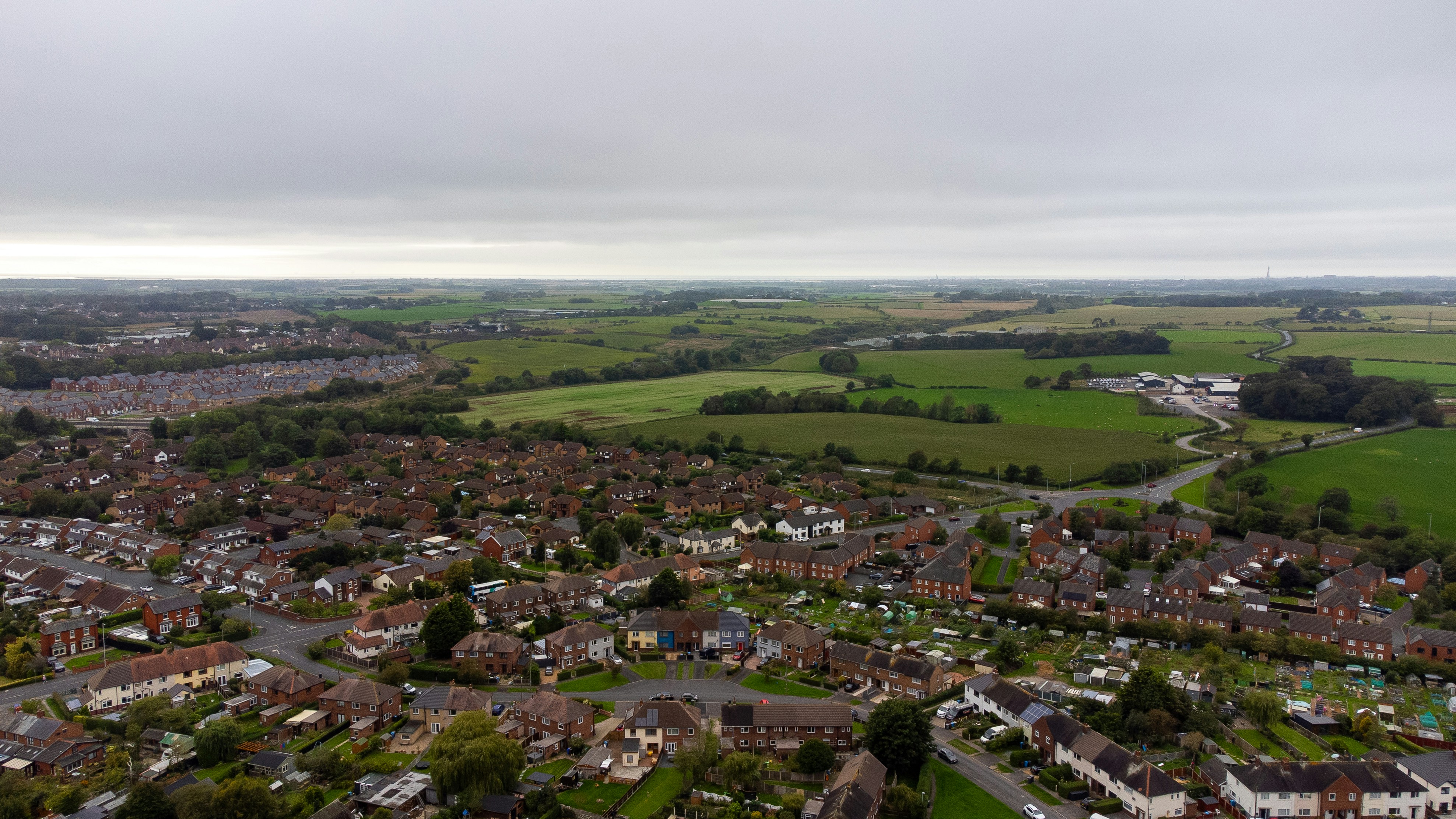 Aerial view of a residential neighborhood surrounded by green fields under a cloudy sky