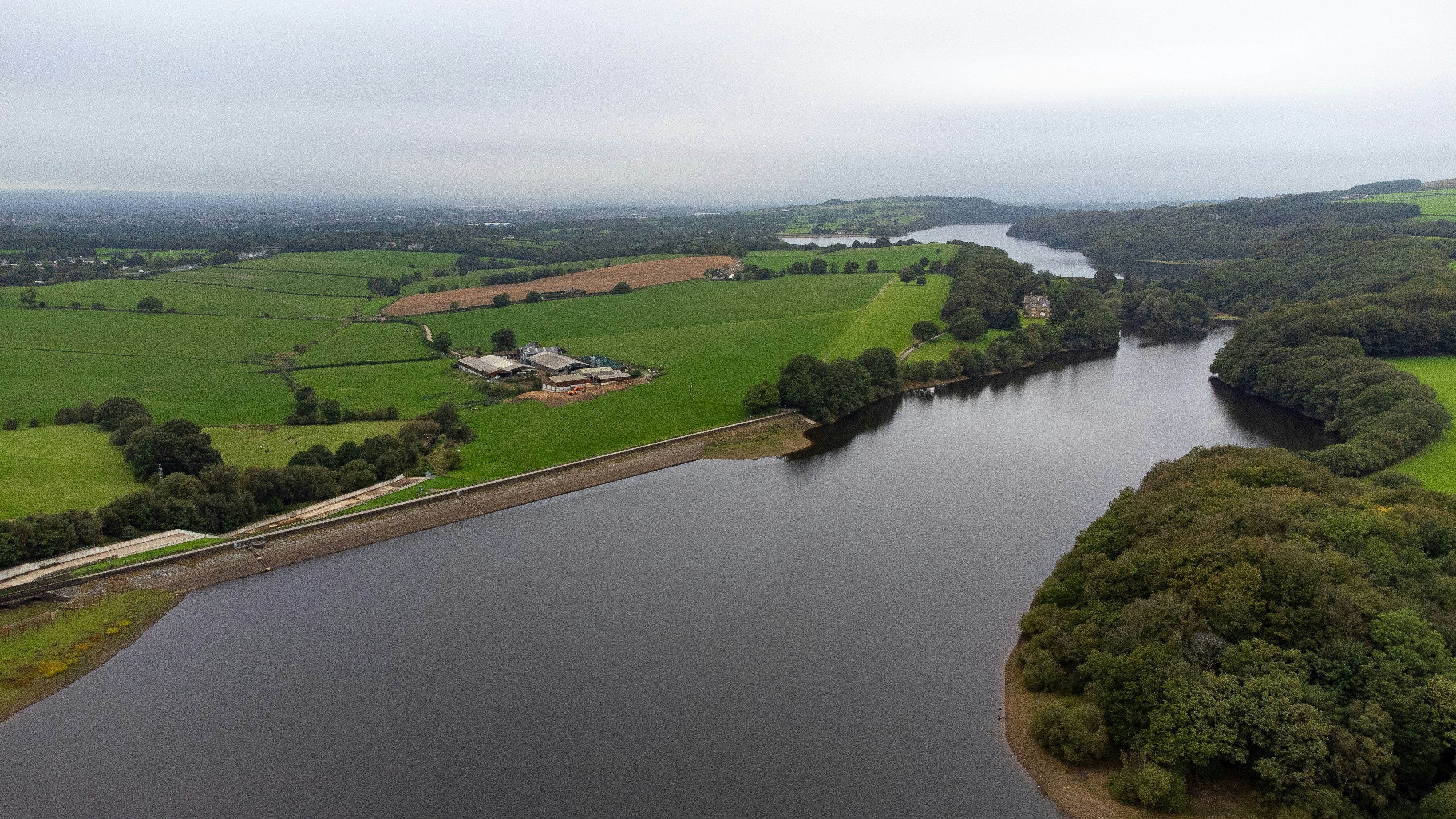 An aerial view of a reservoir bordered by green fields and dense woodland
