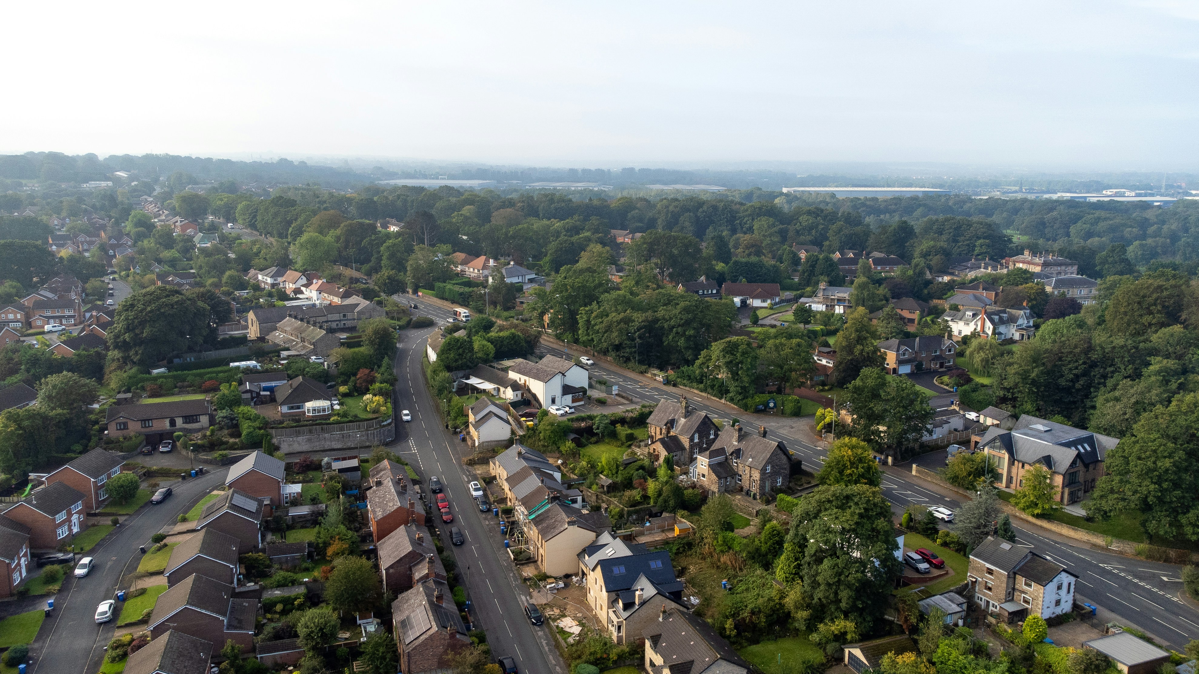 An aerial view of a suburban neighborhood with winding roads and dense green trees