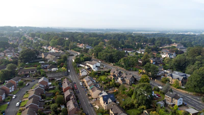 An aerial view of a suburban neighborhood with winding roads and dense green trees