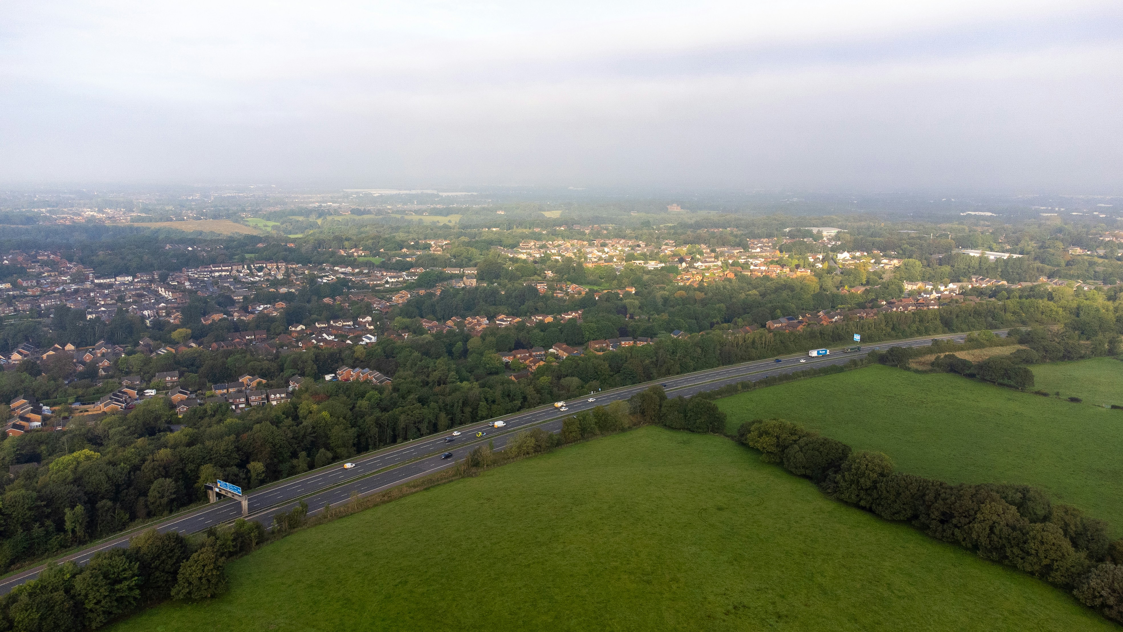 An aerial view of a highway cutting through green fields and suburban housing