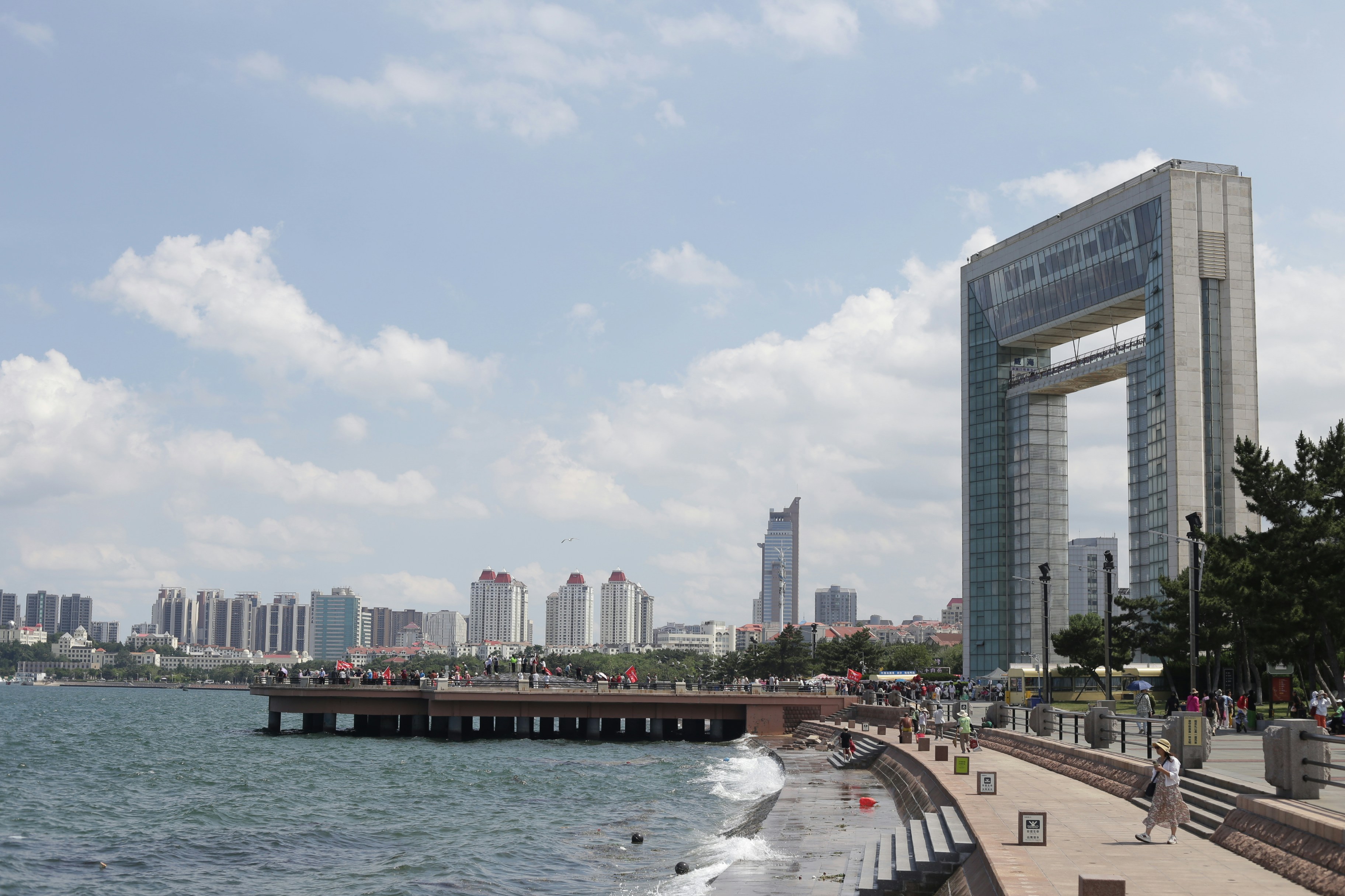 A large stone arch monument on a coastal promenade with a city skyline