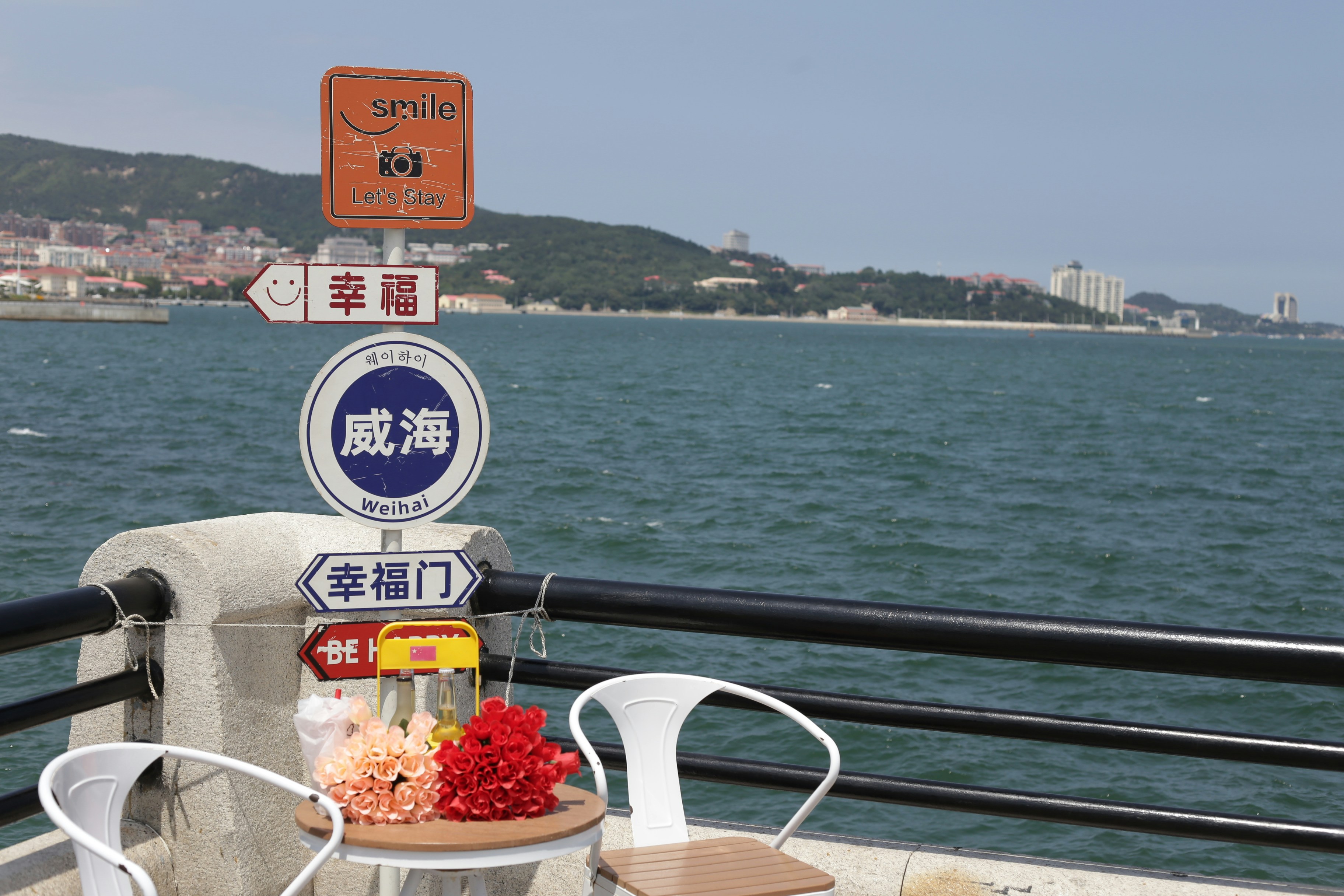 A small table with flowers by a signpost overlooking the sea in Weihai