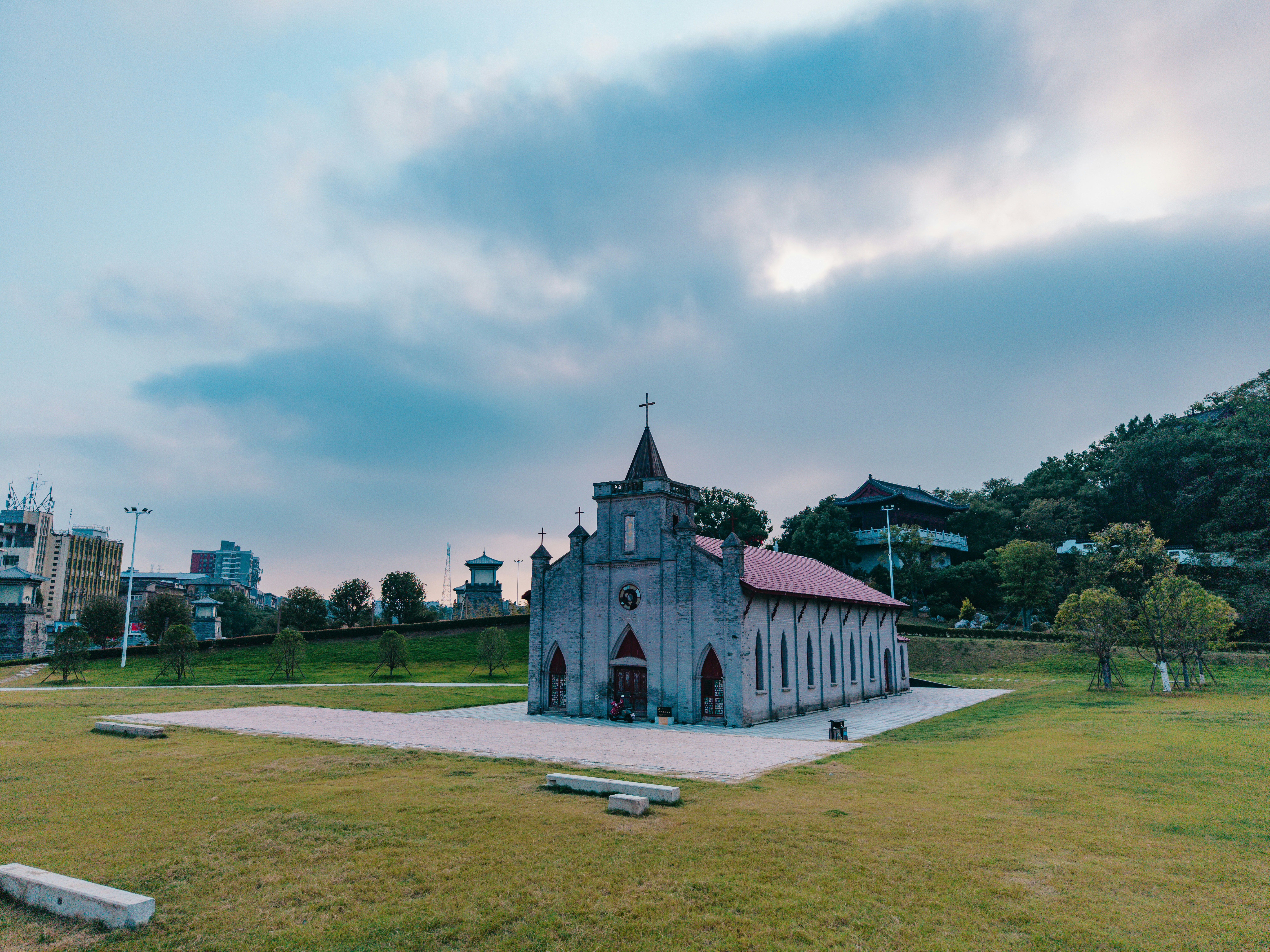 A stone church with a cross on a grassy field under a cloudy sky