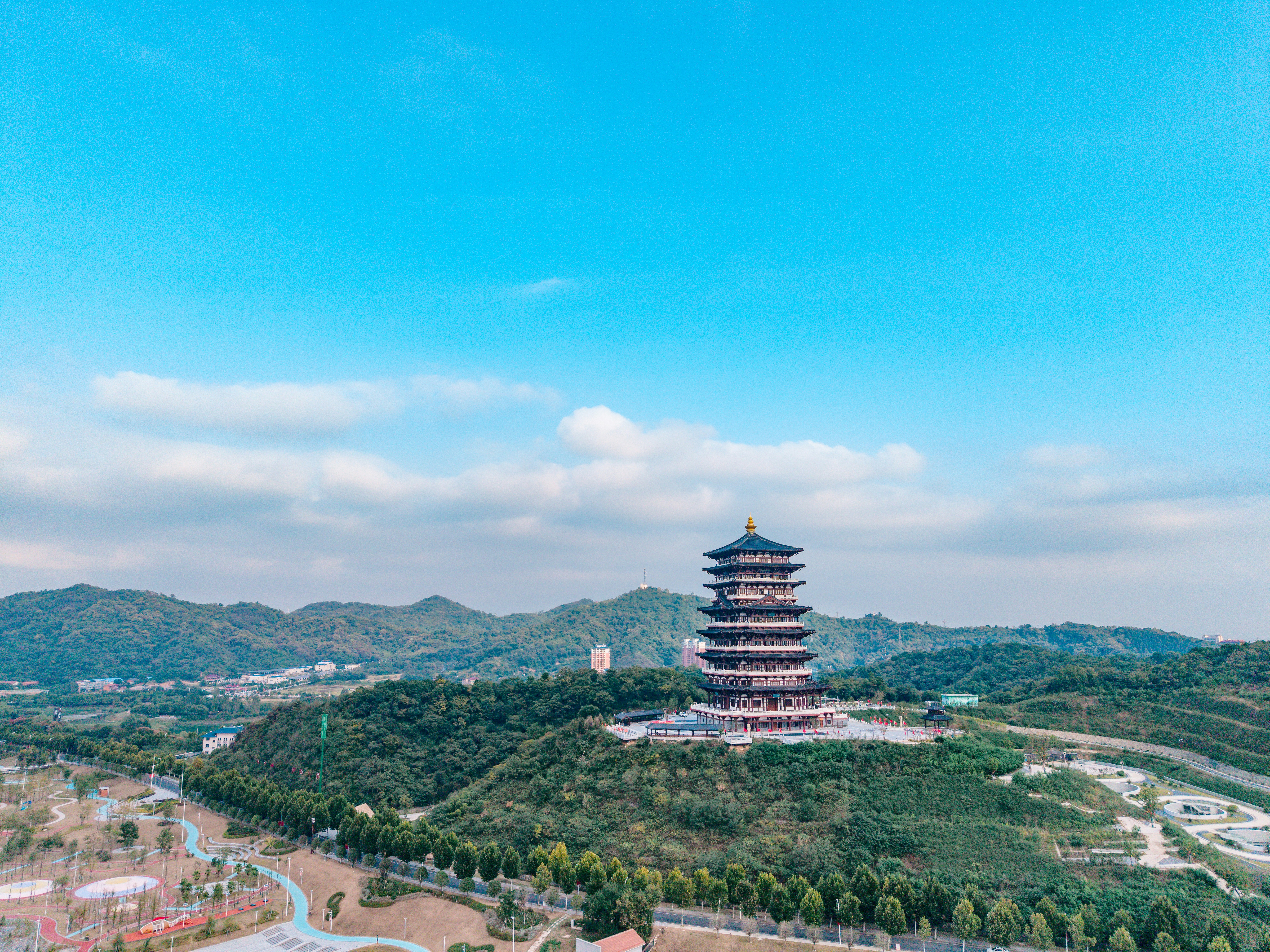 A multi-story pagoda on a green hill overlooking a park and distant mountains