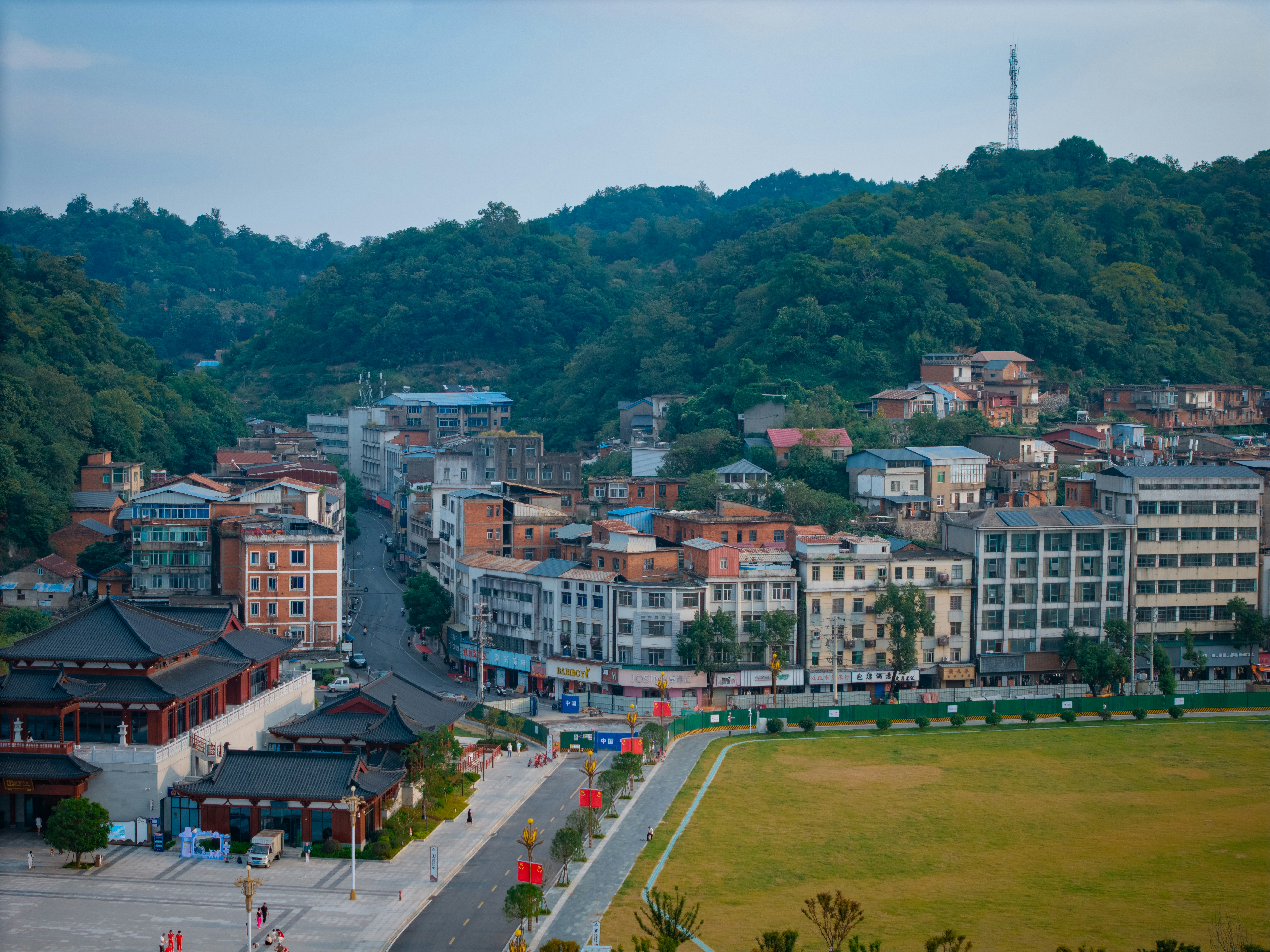 A town with traditional Chinese architecture and modern buildings nestled against a forested mountain