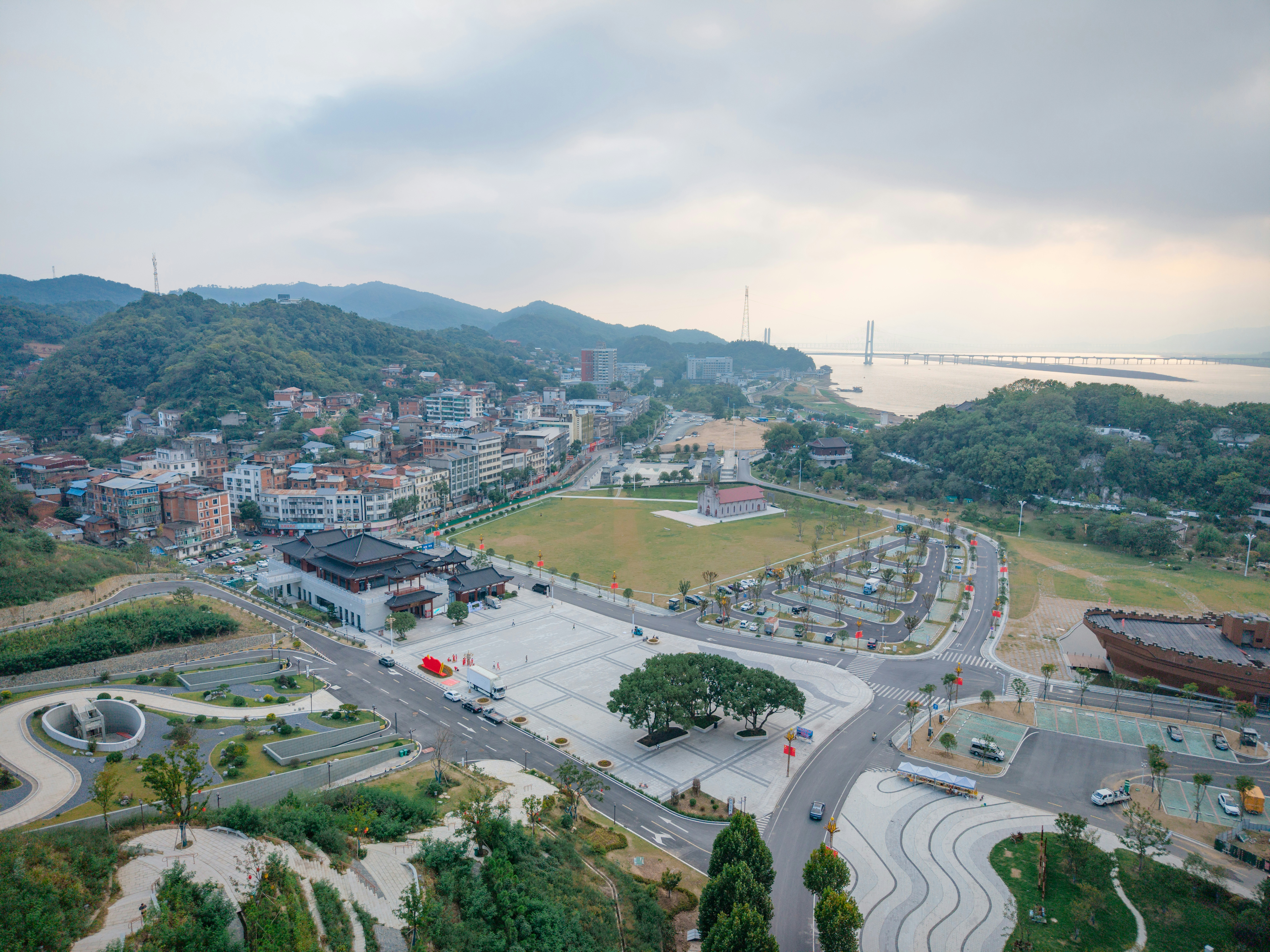Aerial view of a town with a large plaza, green hills, and a bridge