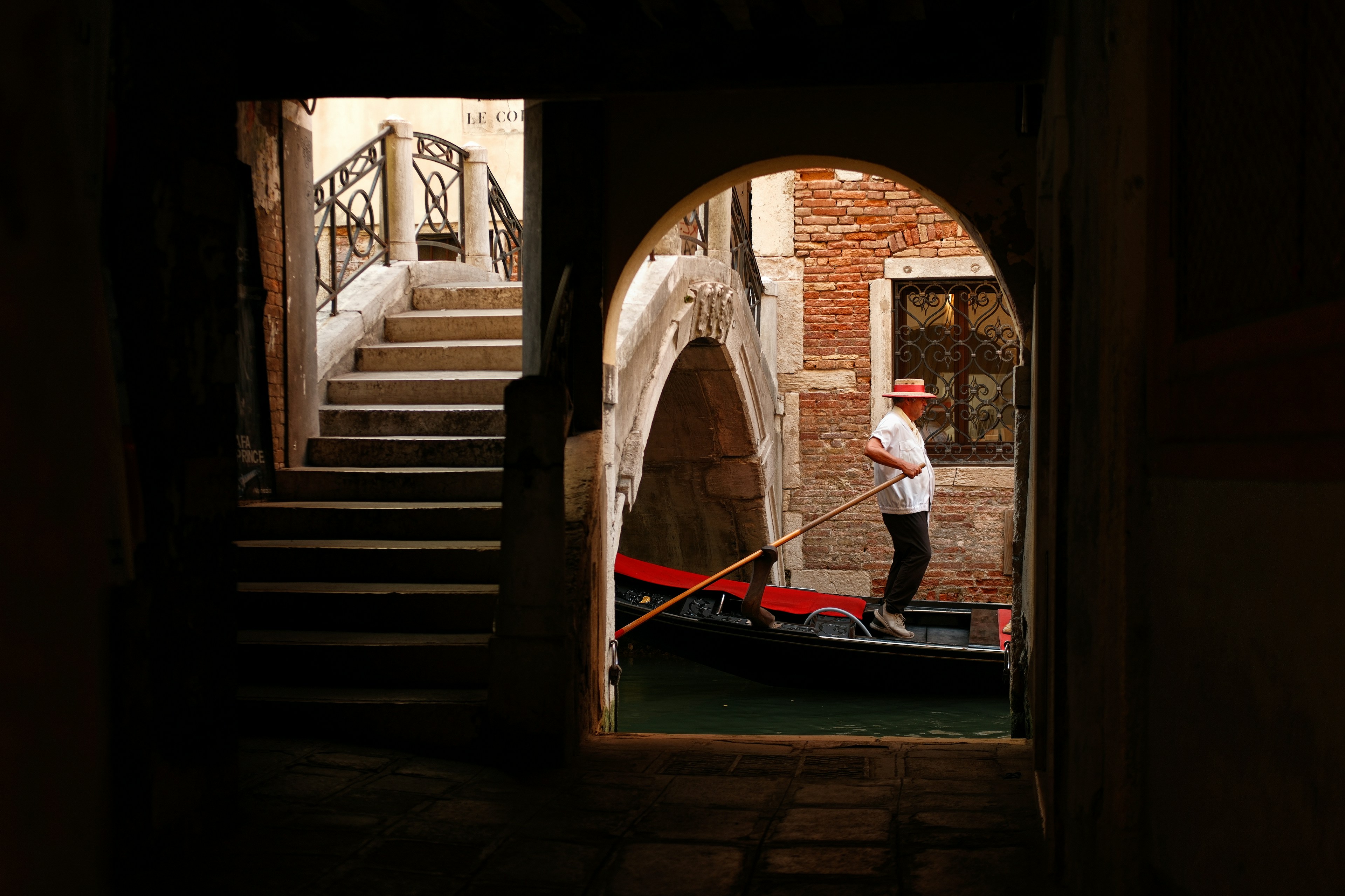 A gondolier in a straw hat rowing a gondola through a canal in Venice